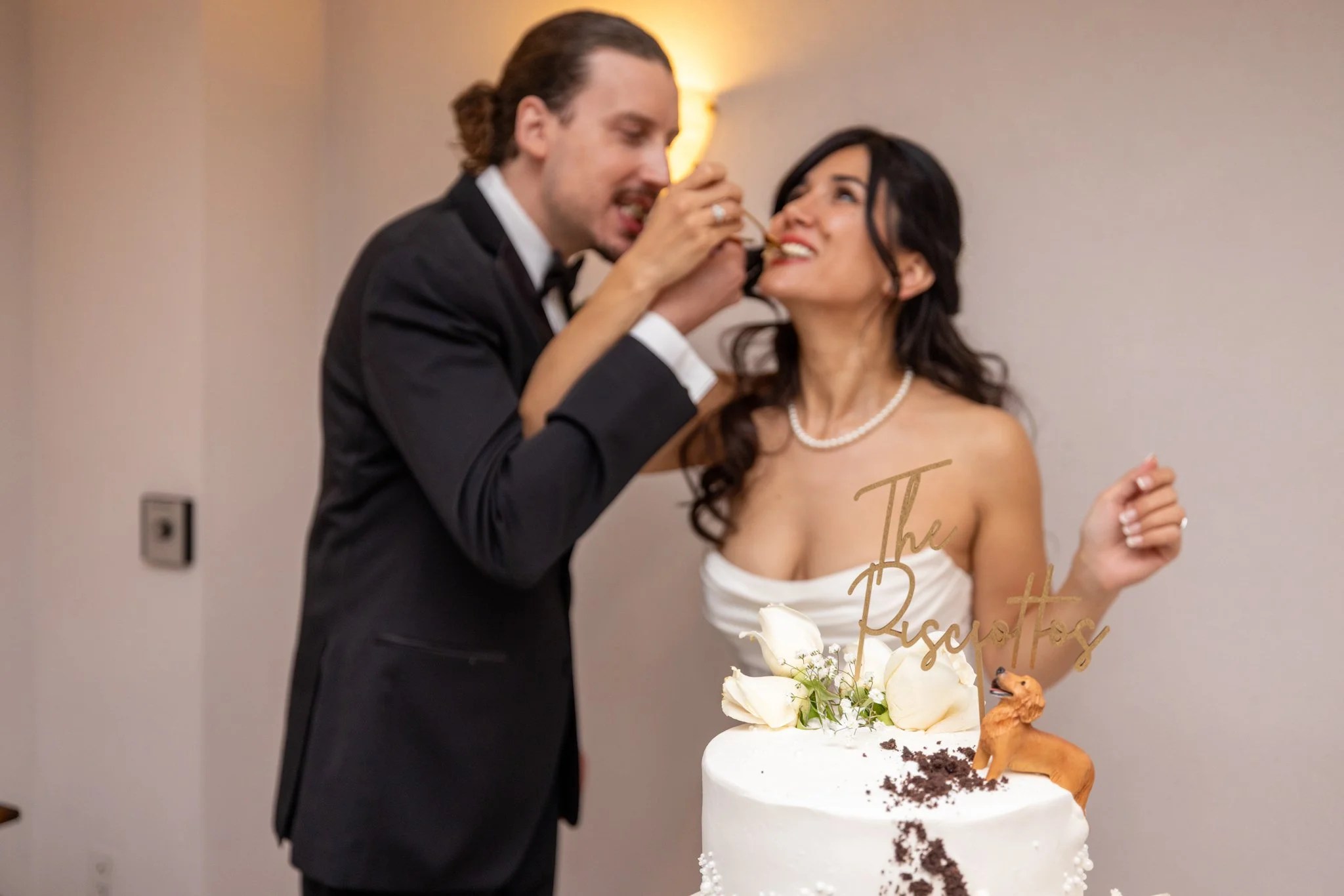Groom playfully feeding the bride a bite of wedding cake during the reception, captured by David Pierre Studio