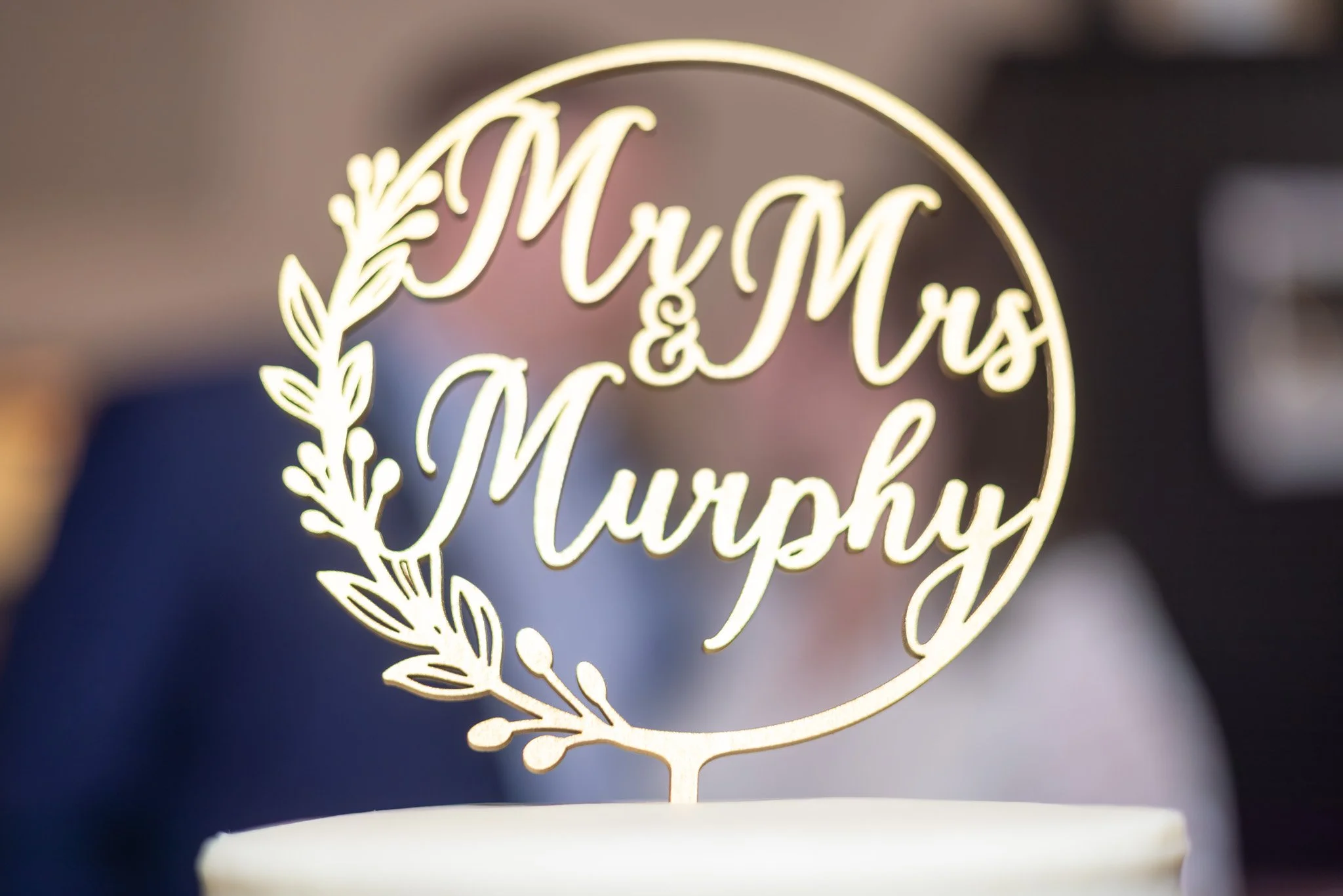 Cake topper with the text "Mr & Mrs Murphy" in cursive, surrounded by a decorative leaf wreath design.