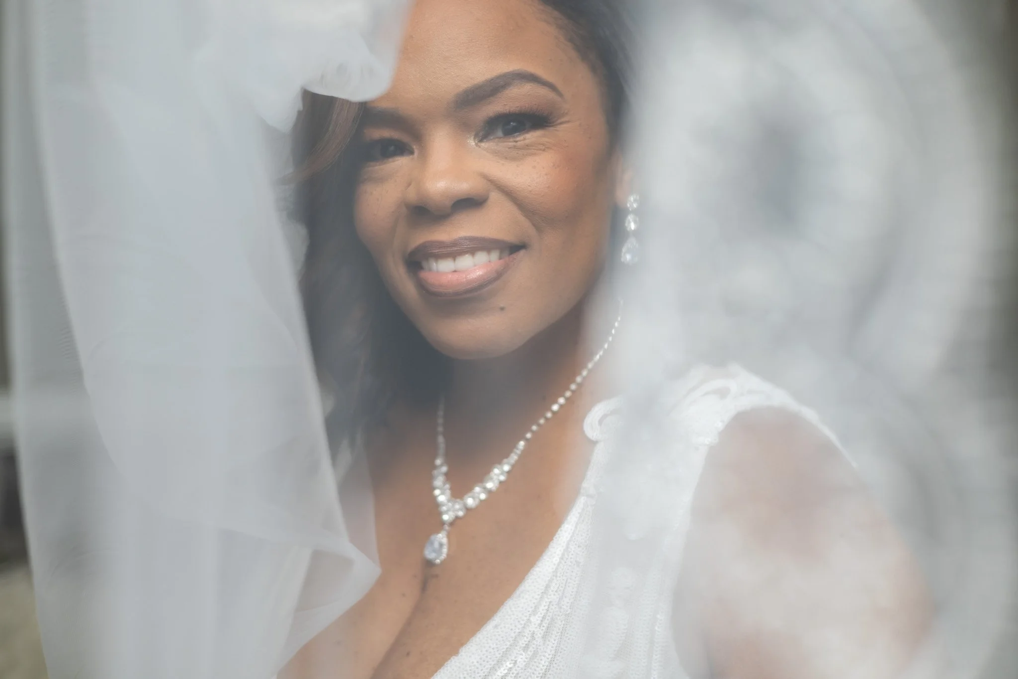 Smiling bride photographed through her veil on her wedding day, captured by David Pierre Studio
