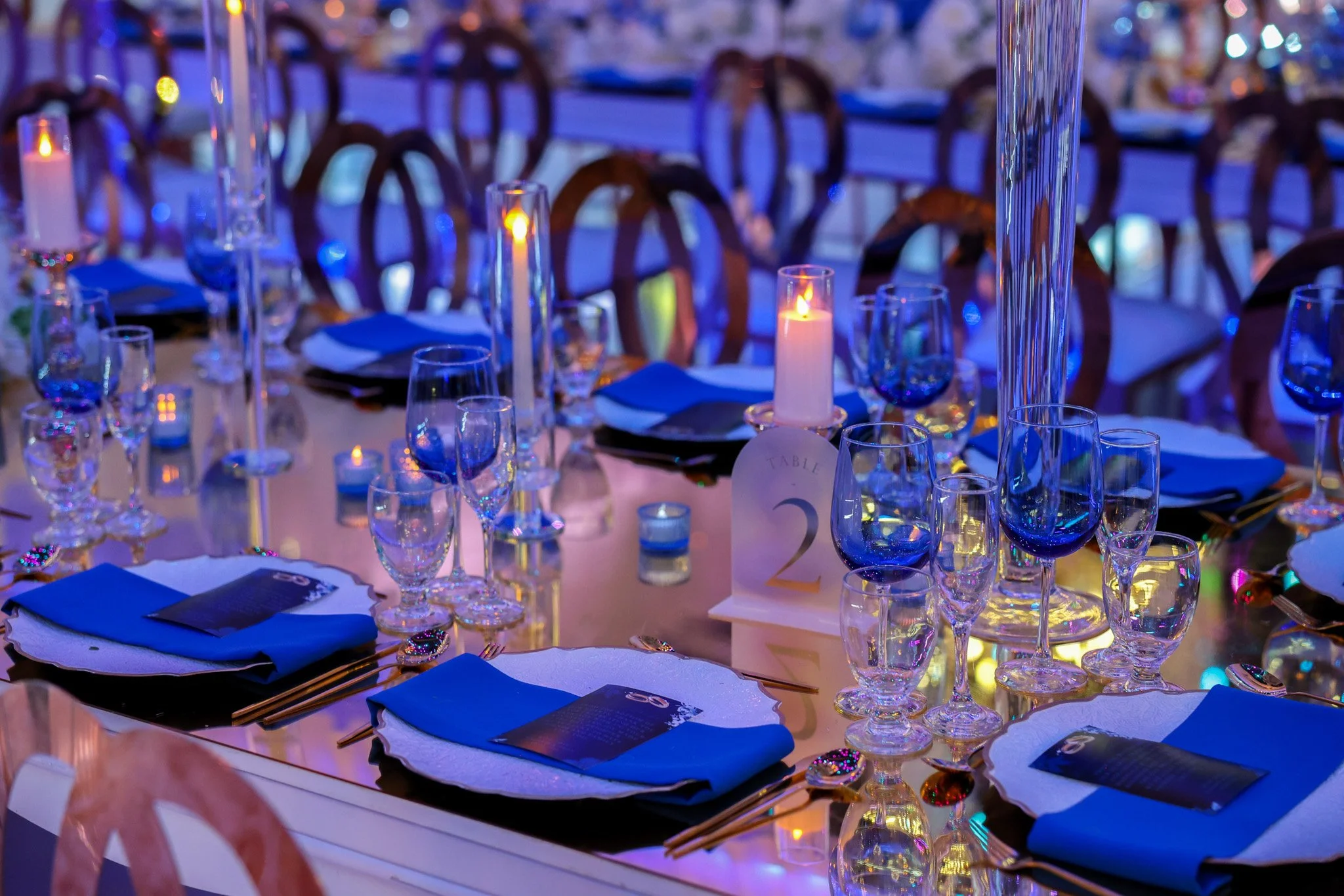 Elegant banquet table setting with blue napkins, wine glasses, and lit candles, decorated for a formal event.
