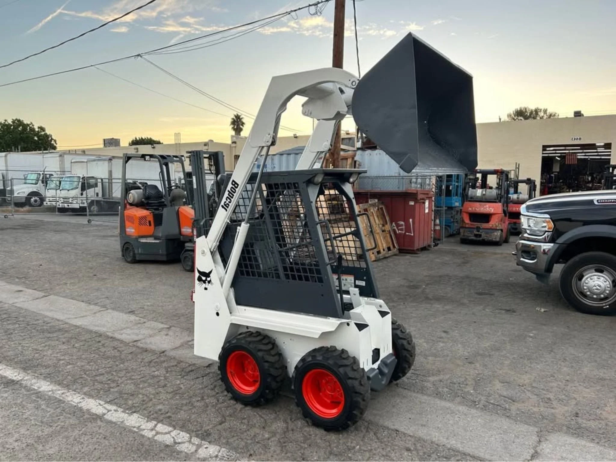 A white Bobcat 443 mini skid steer with large black smooth bucket attachment. Available for rent in Santa Ana, CA only $150 per day.