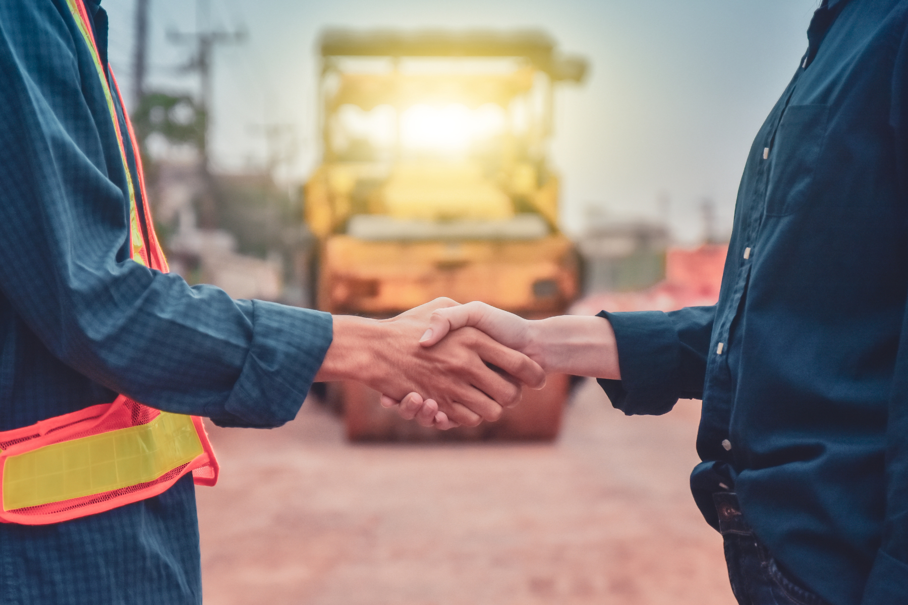 Two people shaking hands in front of a construction vehicle at a construction site, with one person wearing a safety vest. Meaning a rental agreement in Santa Ana, CA