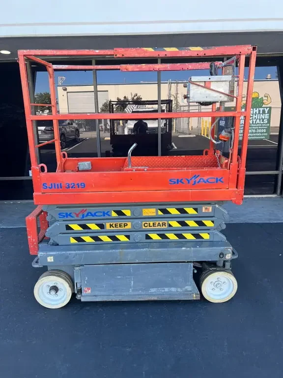 Red and gray Skyjack scissor lift parked outside a building. Available for rent in Santa Ana, CA