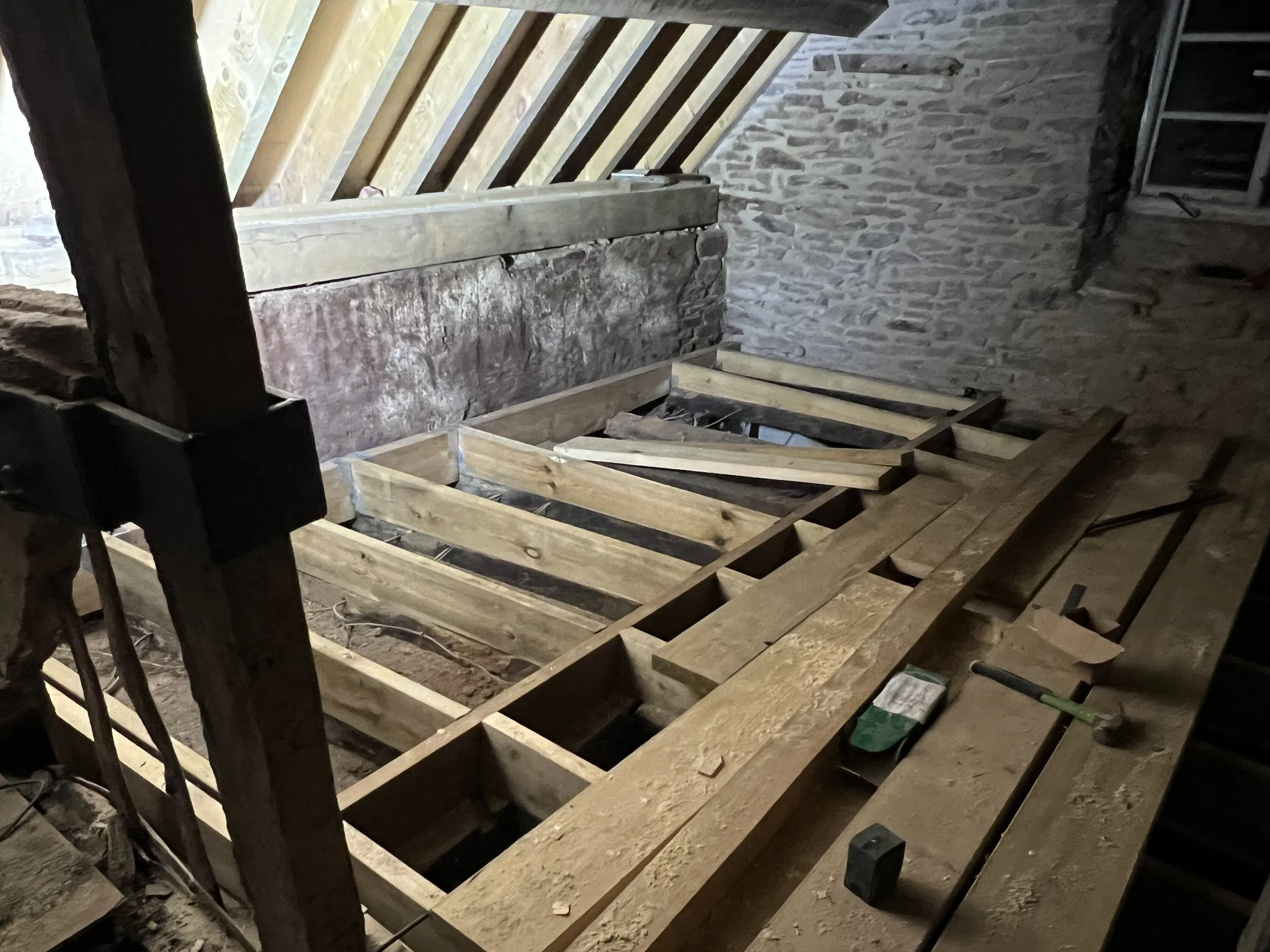 Interior of a building under renovation with exposed brick walls and a wooden framework for a floor or ceiling under construction.