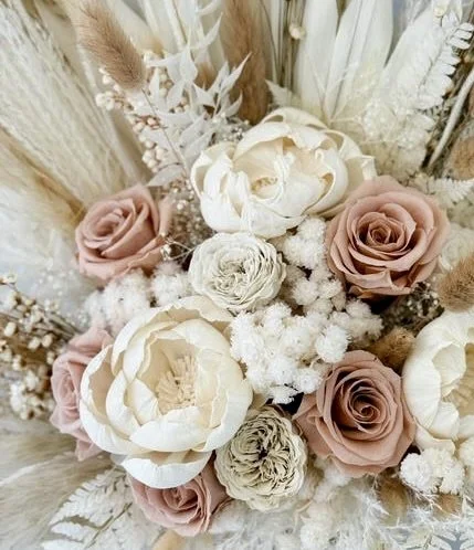 A bouquet of dried and preserved flowers, including beige and pink roses, white blooms, and various textured foliage.