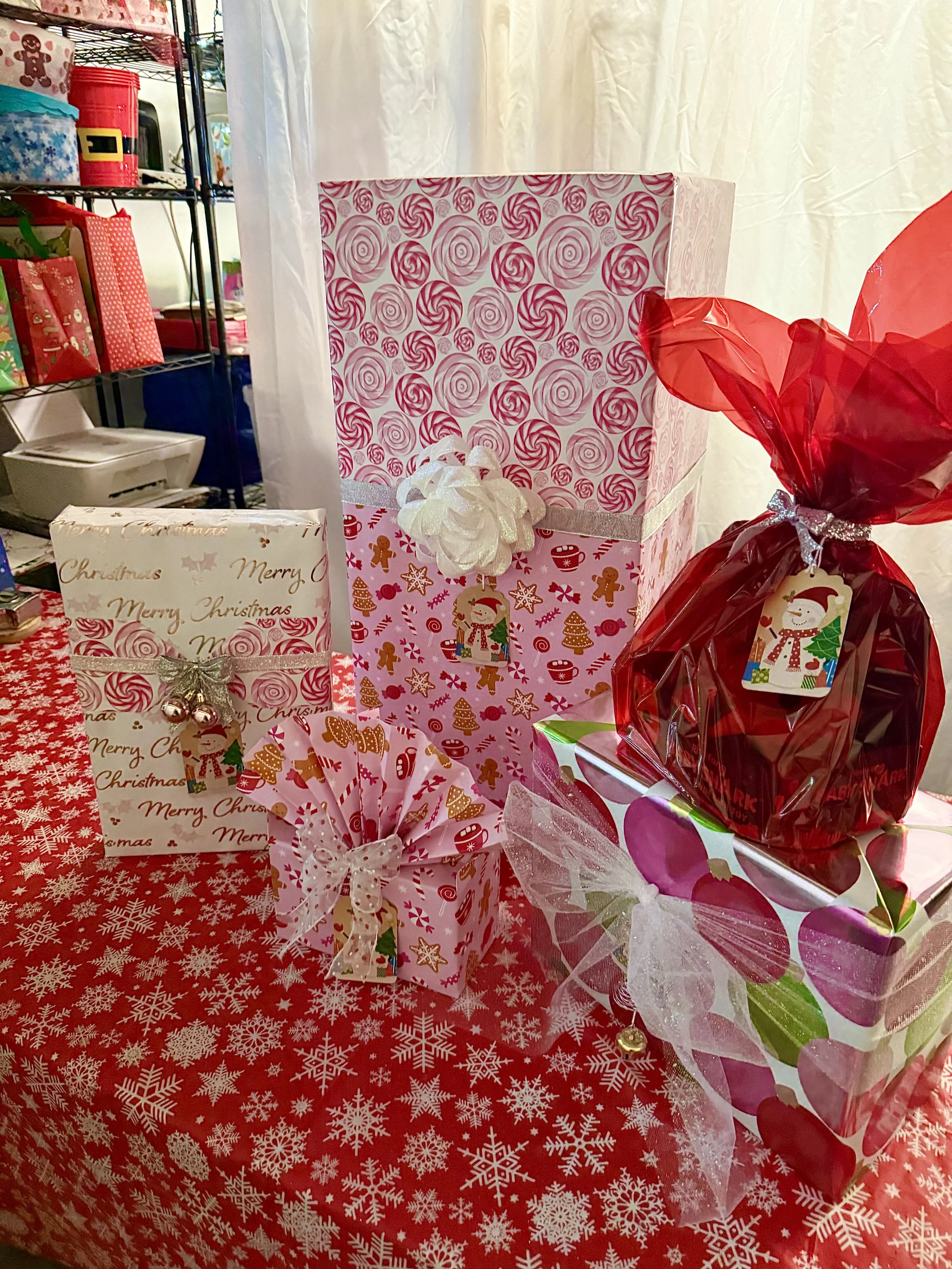 Christmas gift boxes decorated with holiday-themed wrapping paper, ribbons, and bows on a table covered with a red and white snowflake tablecloth.