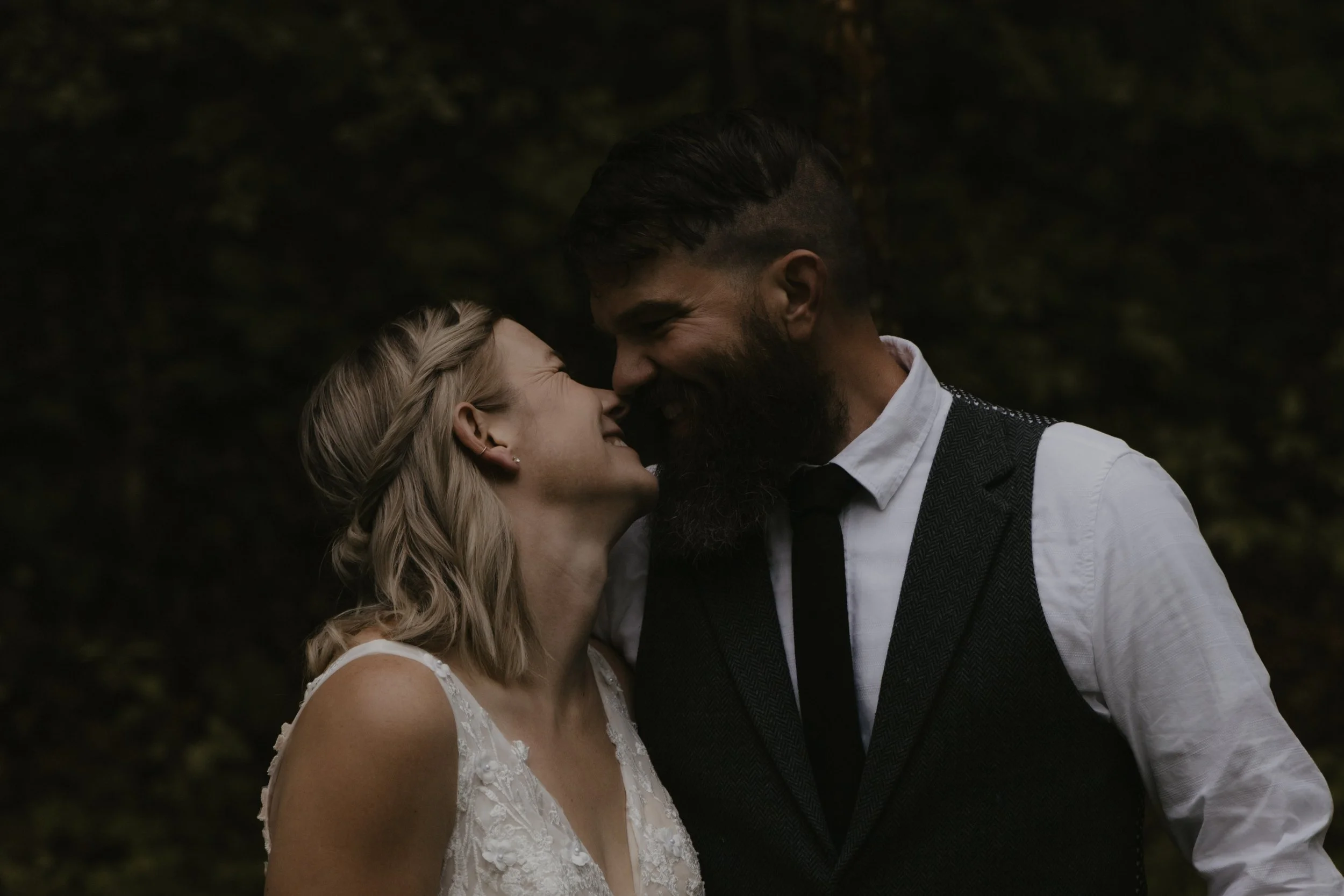 A man and woman are close together, noses touching, smiling in a loving moment outdoors.