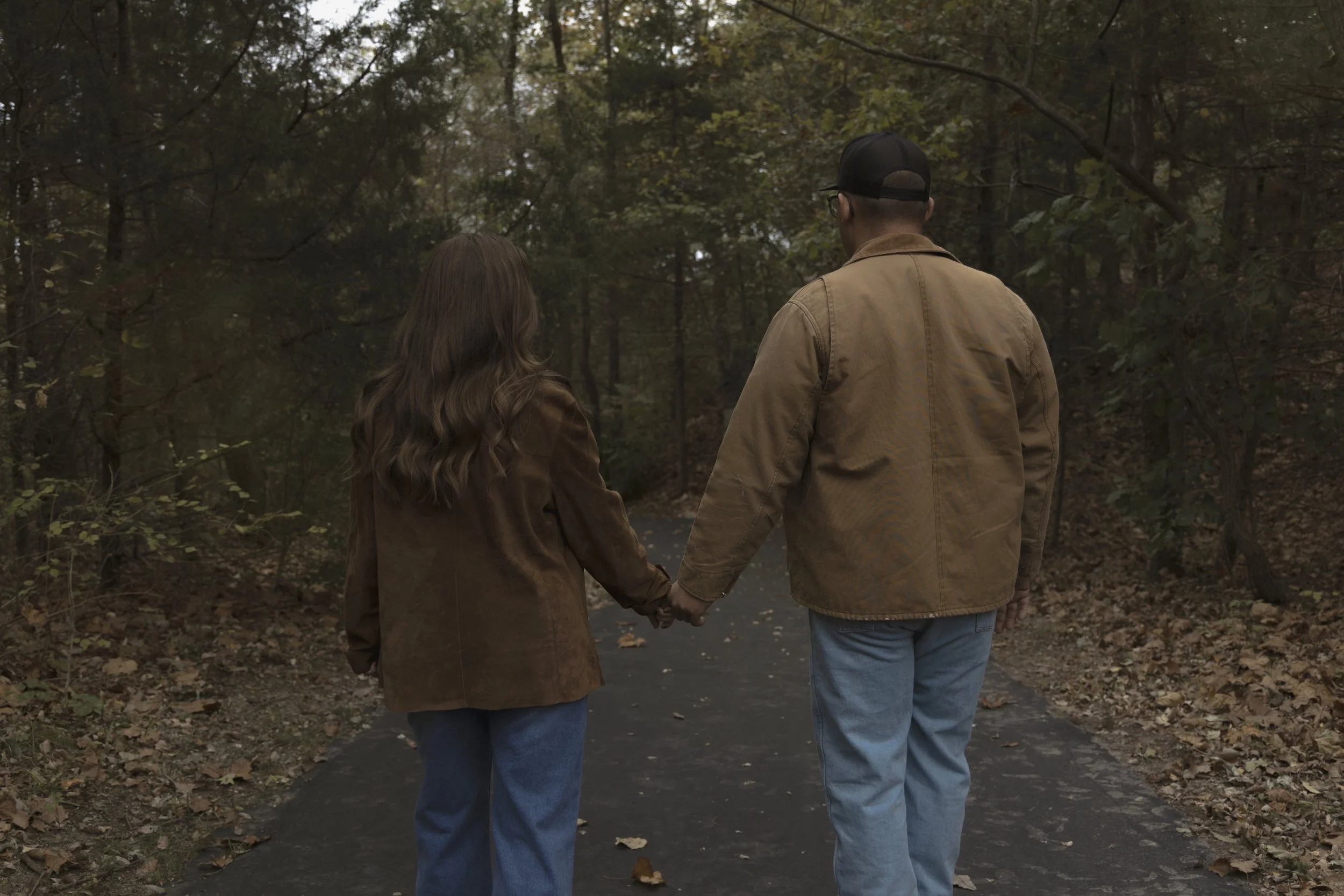 A couple holding hands walking down a wooded trail in fall.