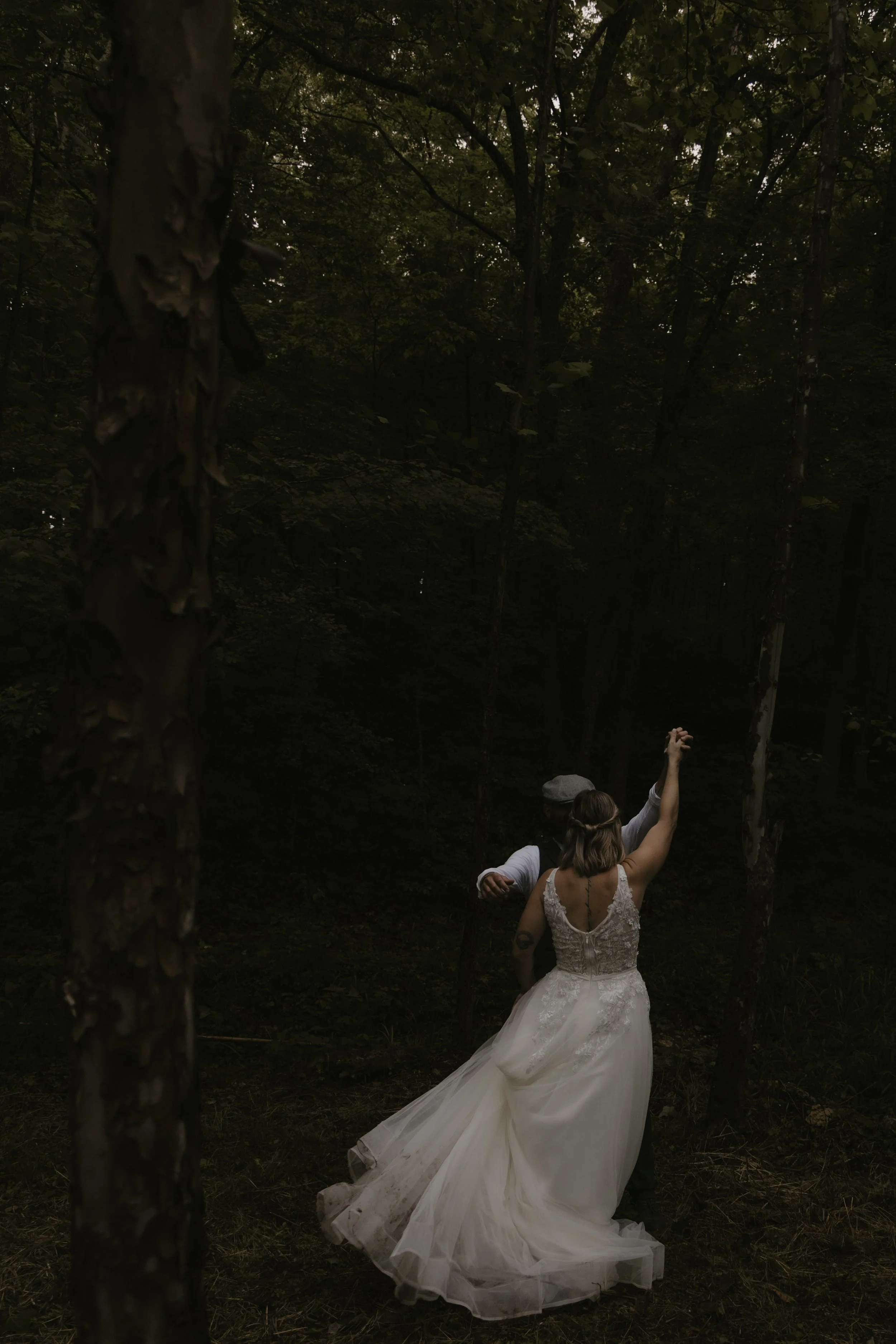 A bride and groom dancing in a dark, forested area during a wedding, with the bride wearing a white wedding gown and the groom in a dark suit.