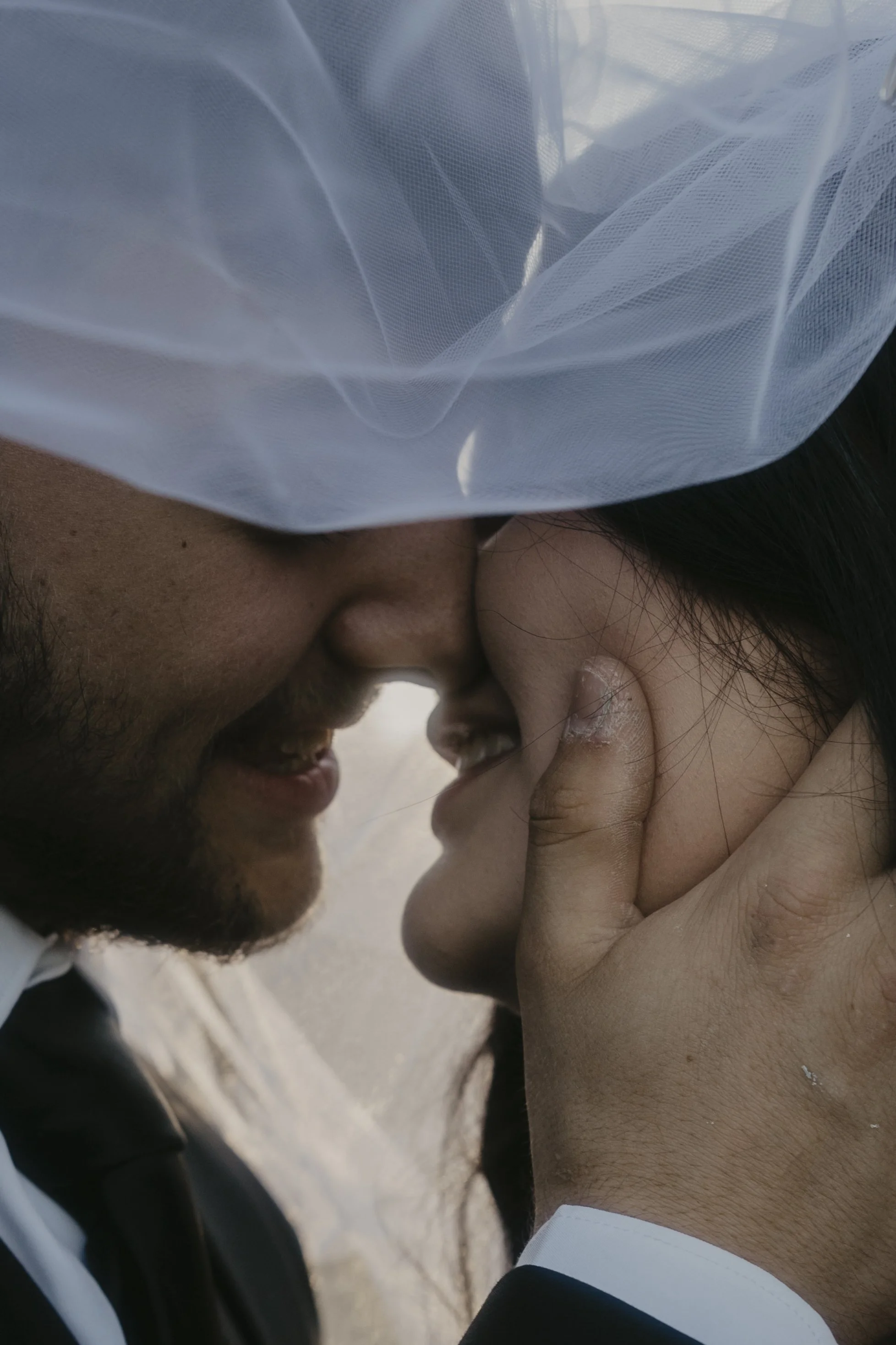 Close-up of a couple touching noses, with the man gently holding the woman's face, both smiling softly, in a romantic moment.
