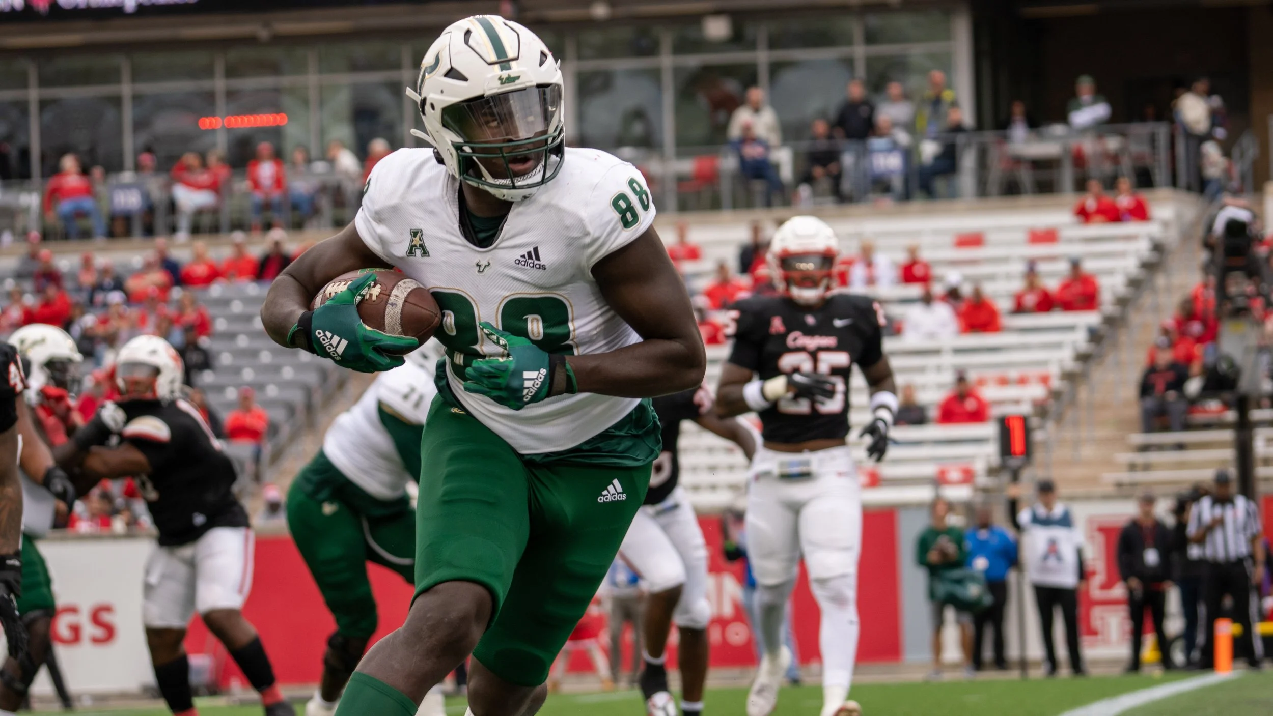 An American football player wearing a white and green uniform running with the ball during a game at a stadium with spectators.