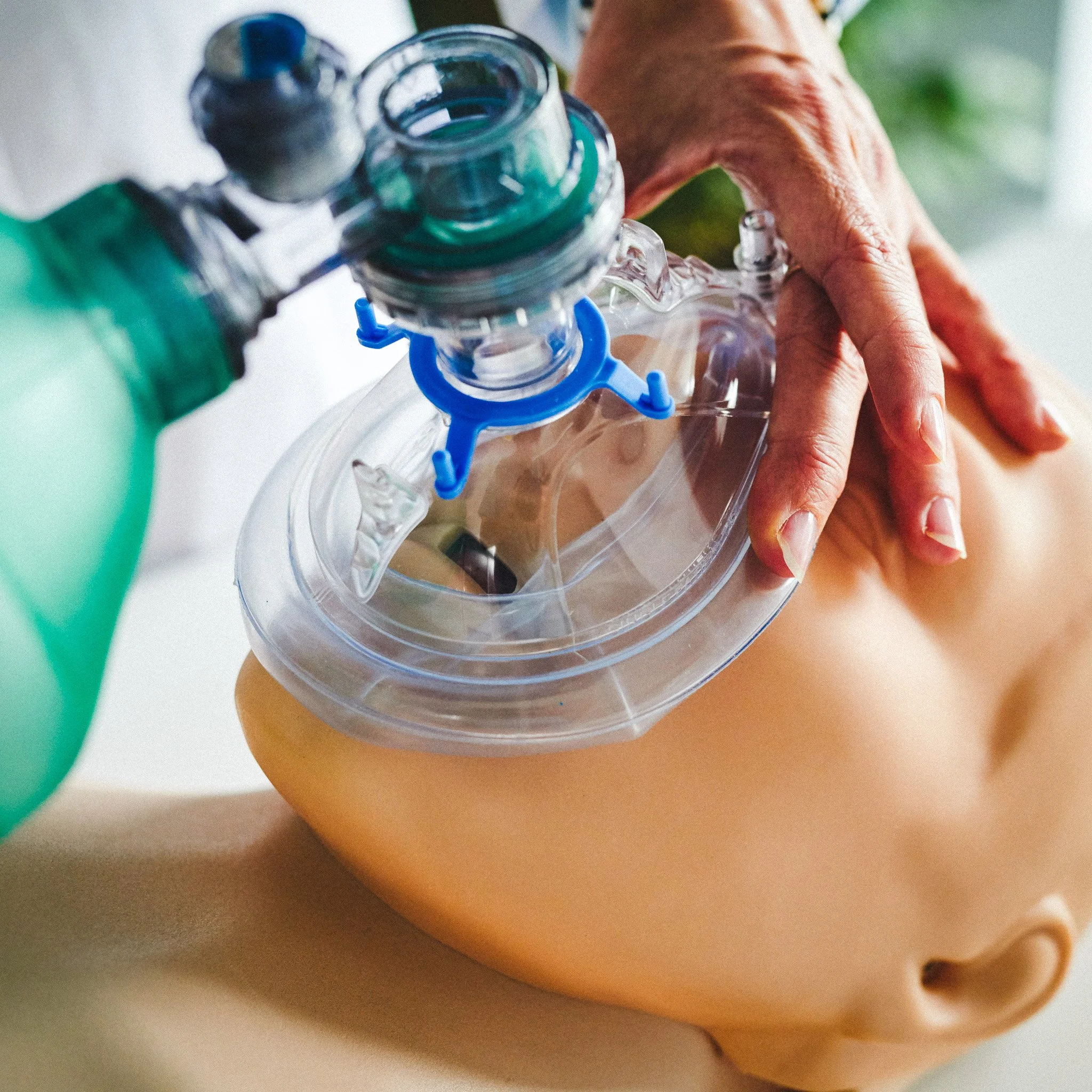 A person performing CPR on a mannequin, utilizing a bag-valve mask device for artificial respiration.