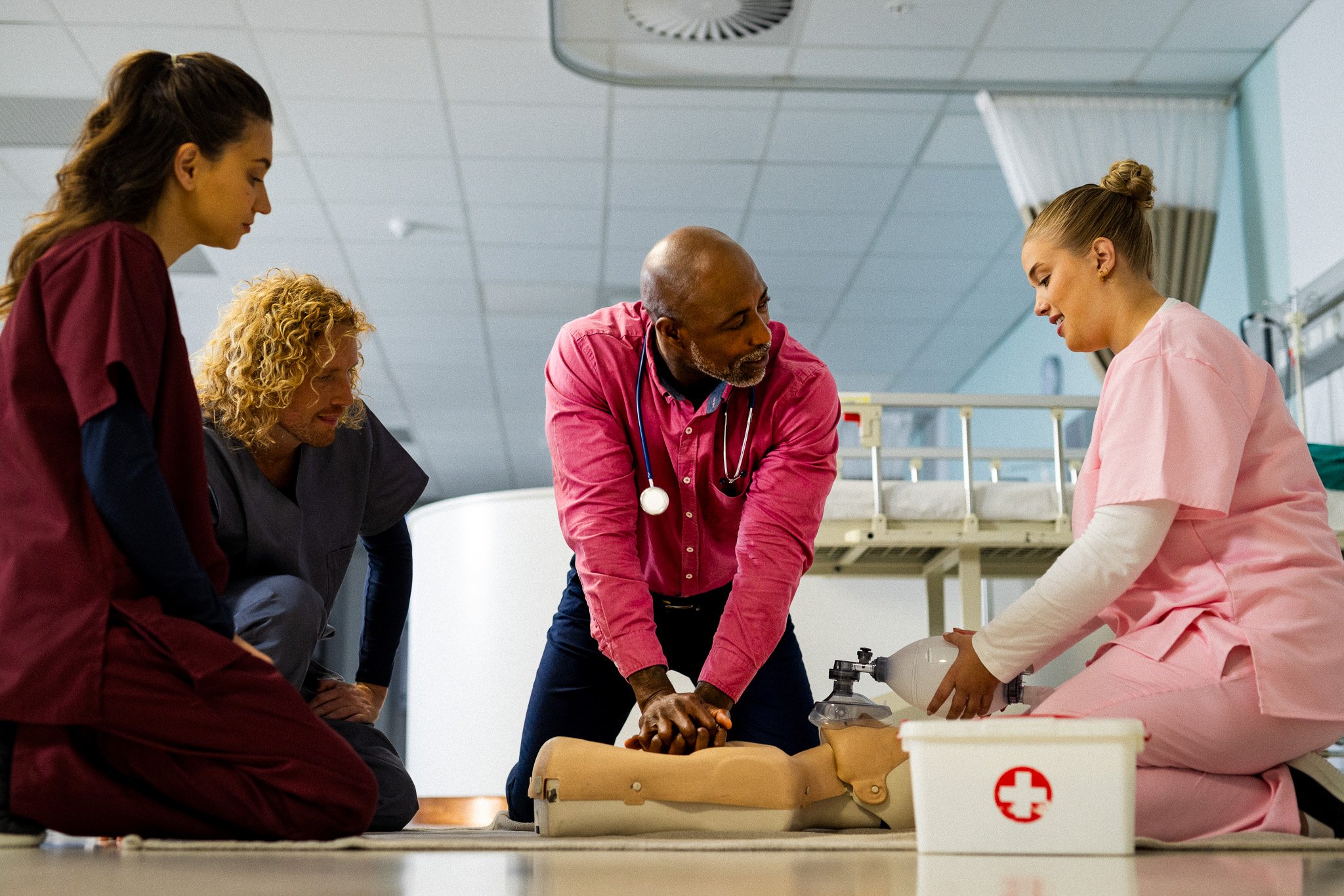 Medical students practicing CPR on a mannequin in a hospital classroom, with instructor guiding them.