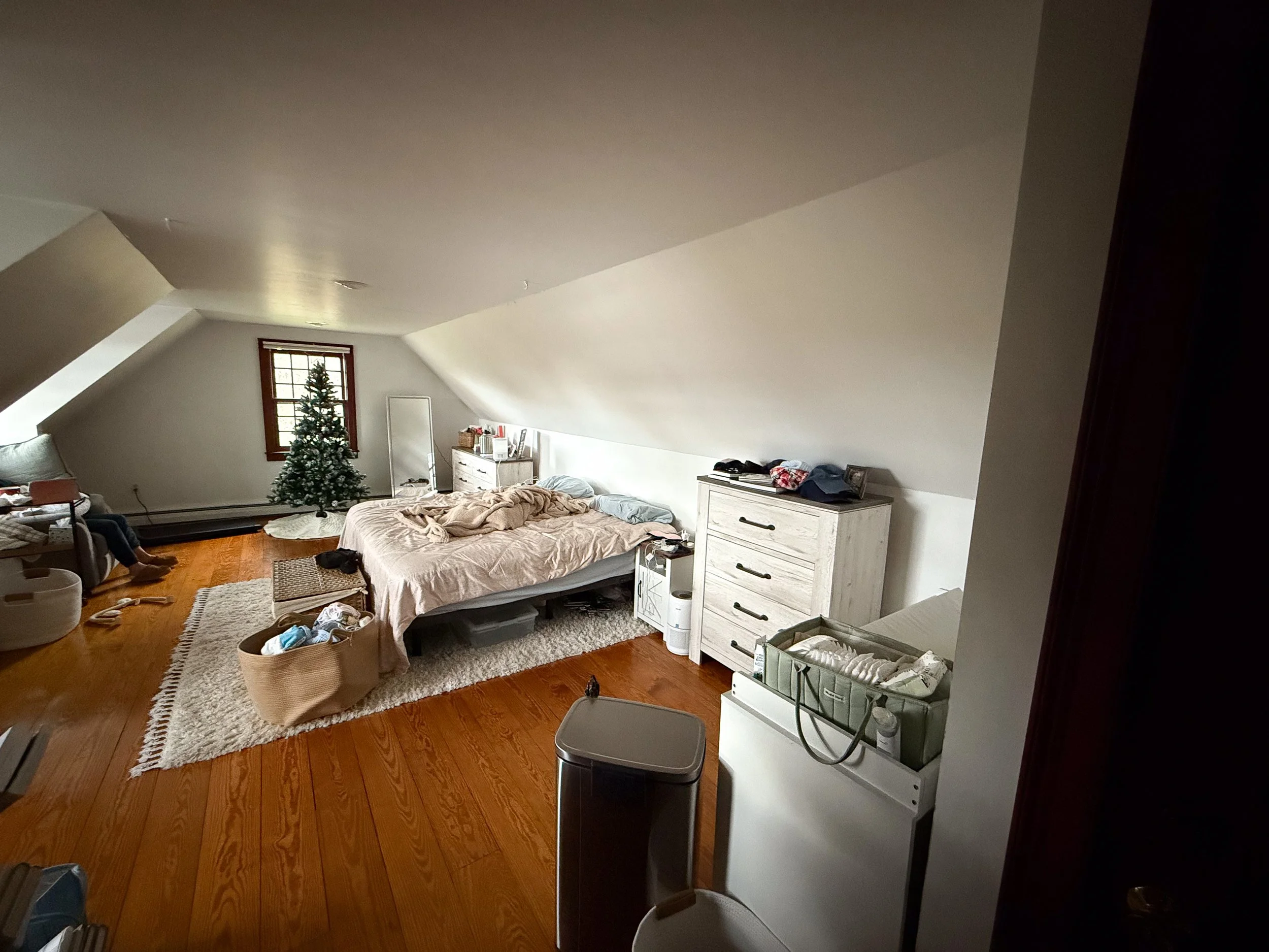 Before photo of a lived-in primary bedroom with baby items, laundry bins, and holiday décor prior to tidying for a lifestyle family photo session.