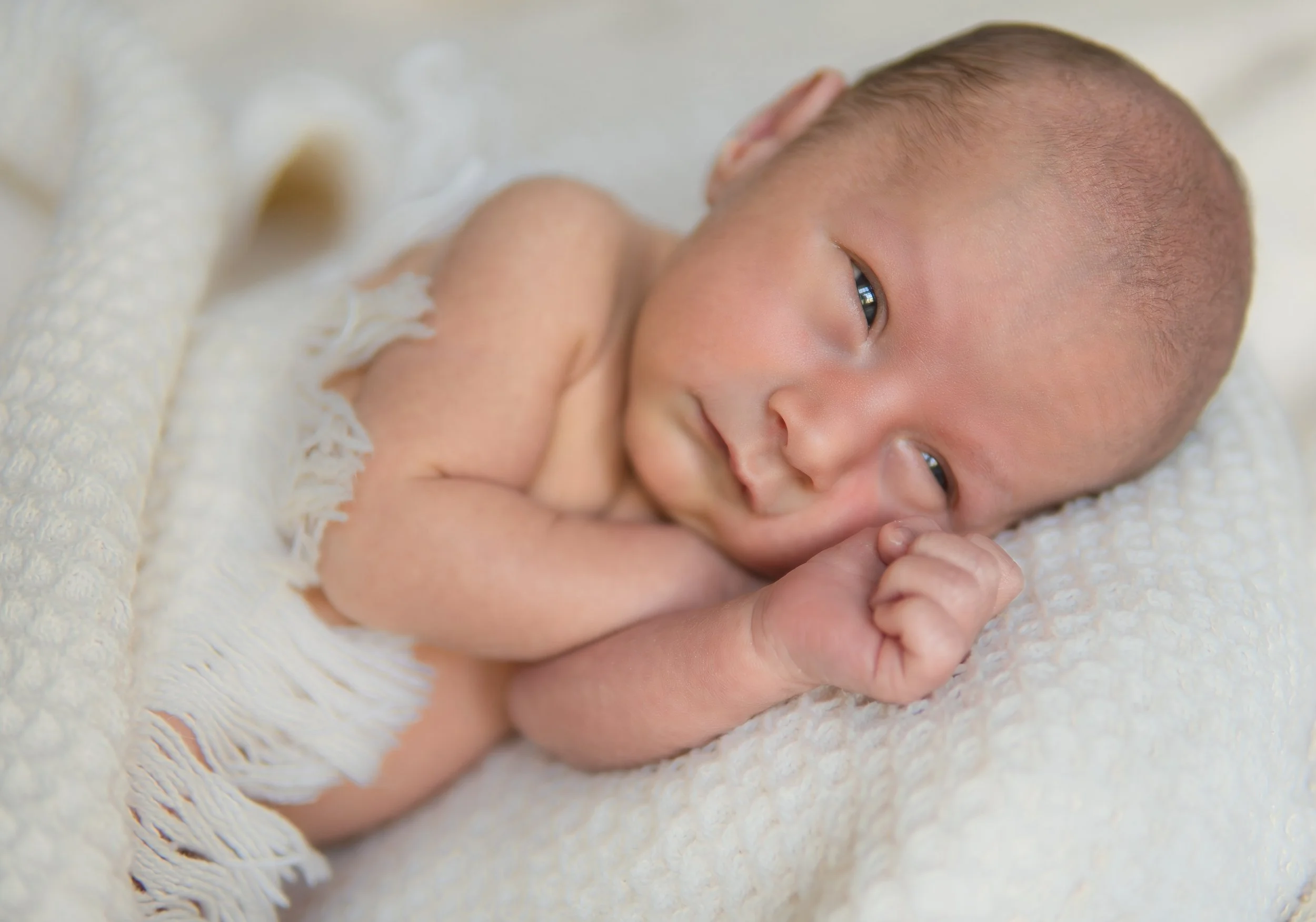 Newborn baby lying awake on a soft white textured blanket during an in-home lifestyle newborn session in Central Massachusetts.