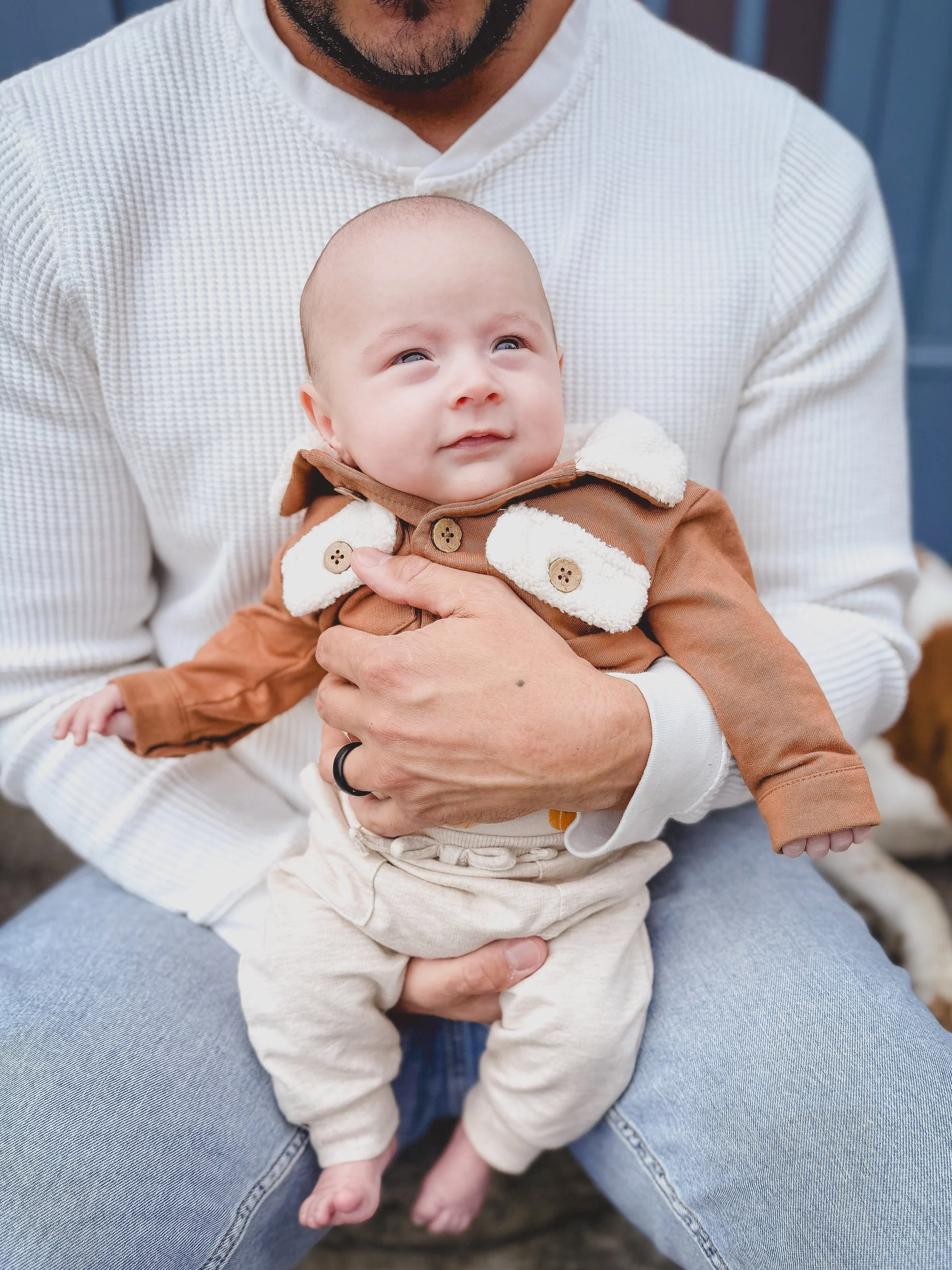 A man holding a baby outside, with a blue background, both dressed in warm clothing.