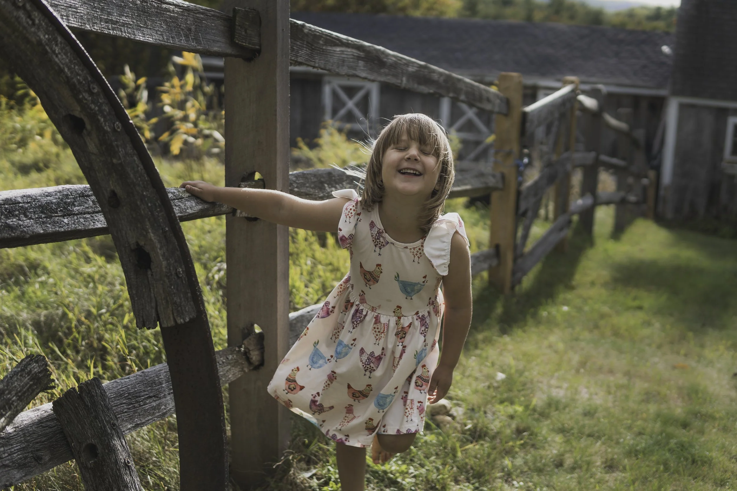 Young girl laughing and running along a rustic fence during a natural outdoor family photography session in Worcester Massachusetts.
