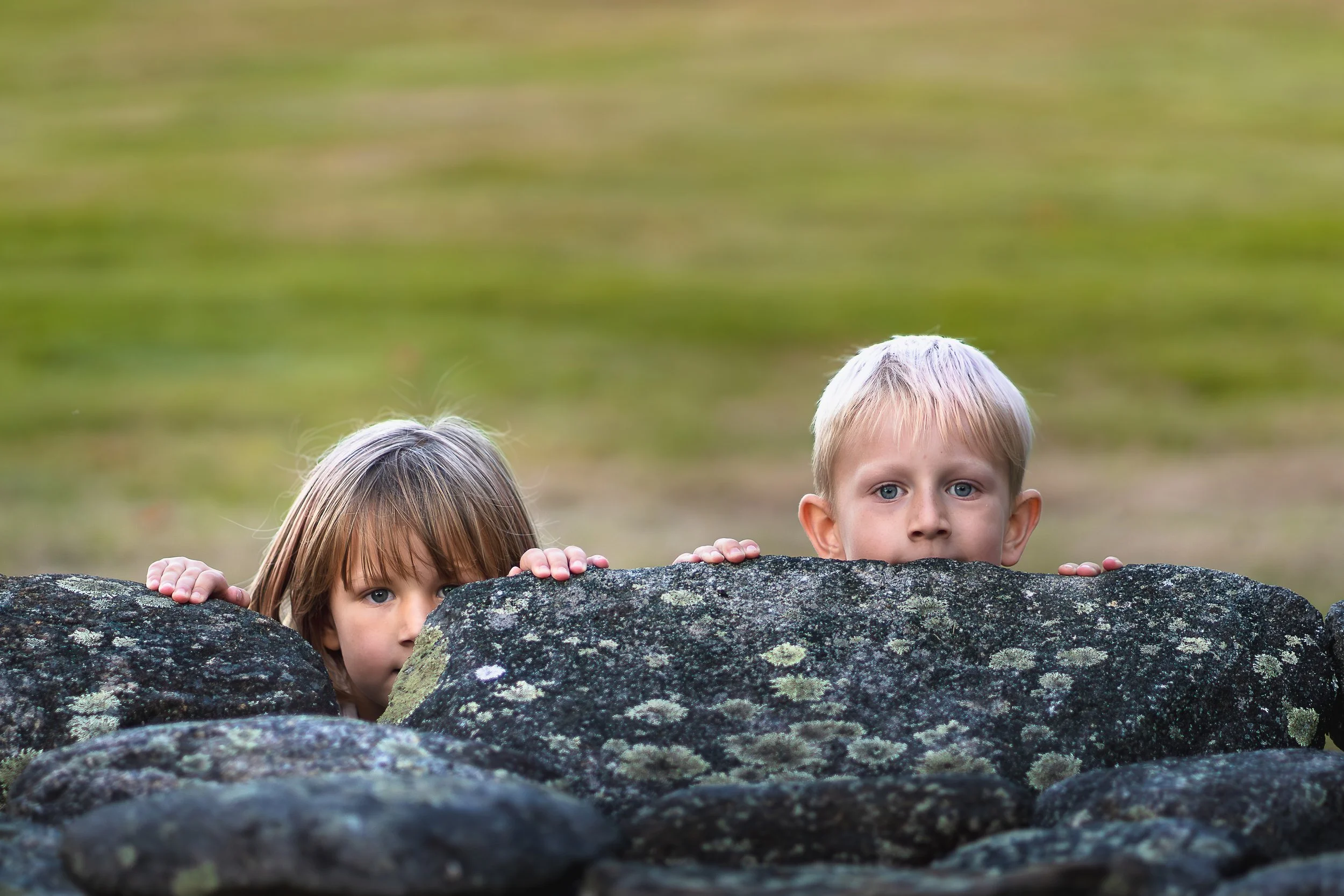 Children peeking over a stone wall during playful family photo session in New England.