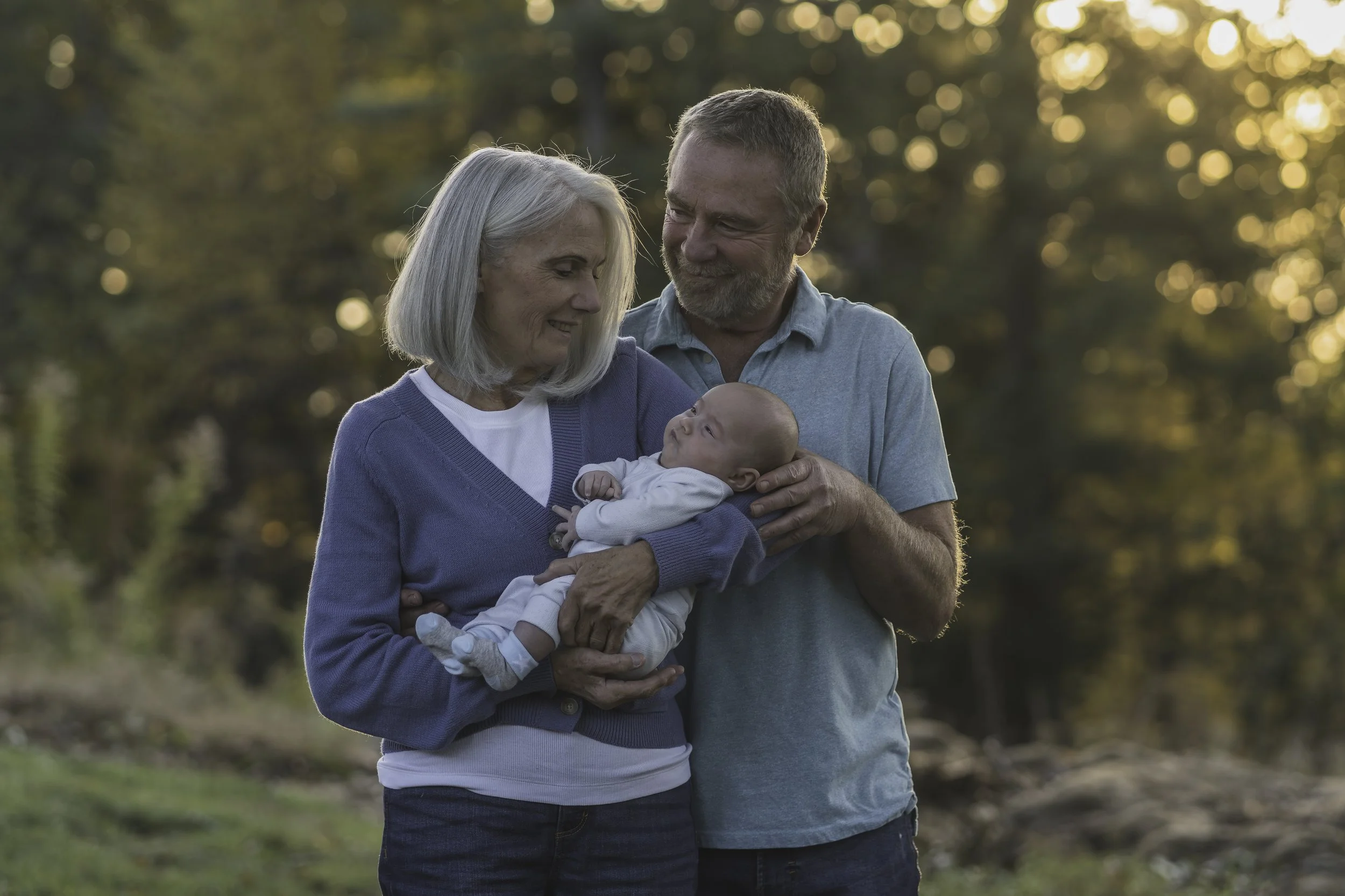 Grandparents holding their newborn grandchild during a golden hour family session in Central Massachusetts, capturing three generations of love.