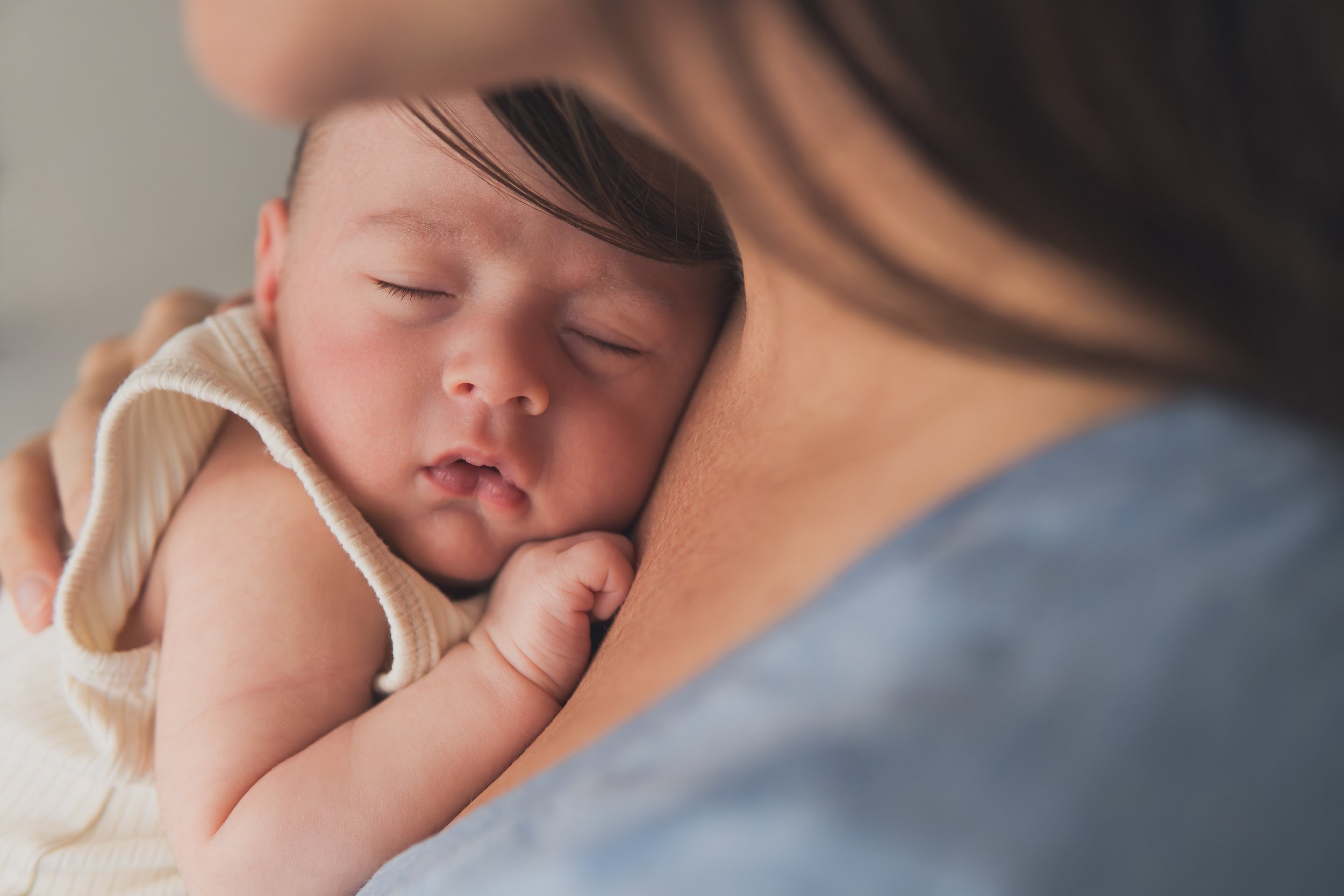 A close-up of a newborn baby with eyes closed, resting on moms shoulder. 
