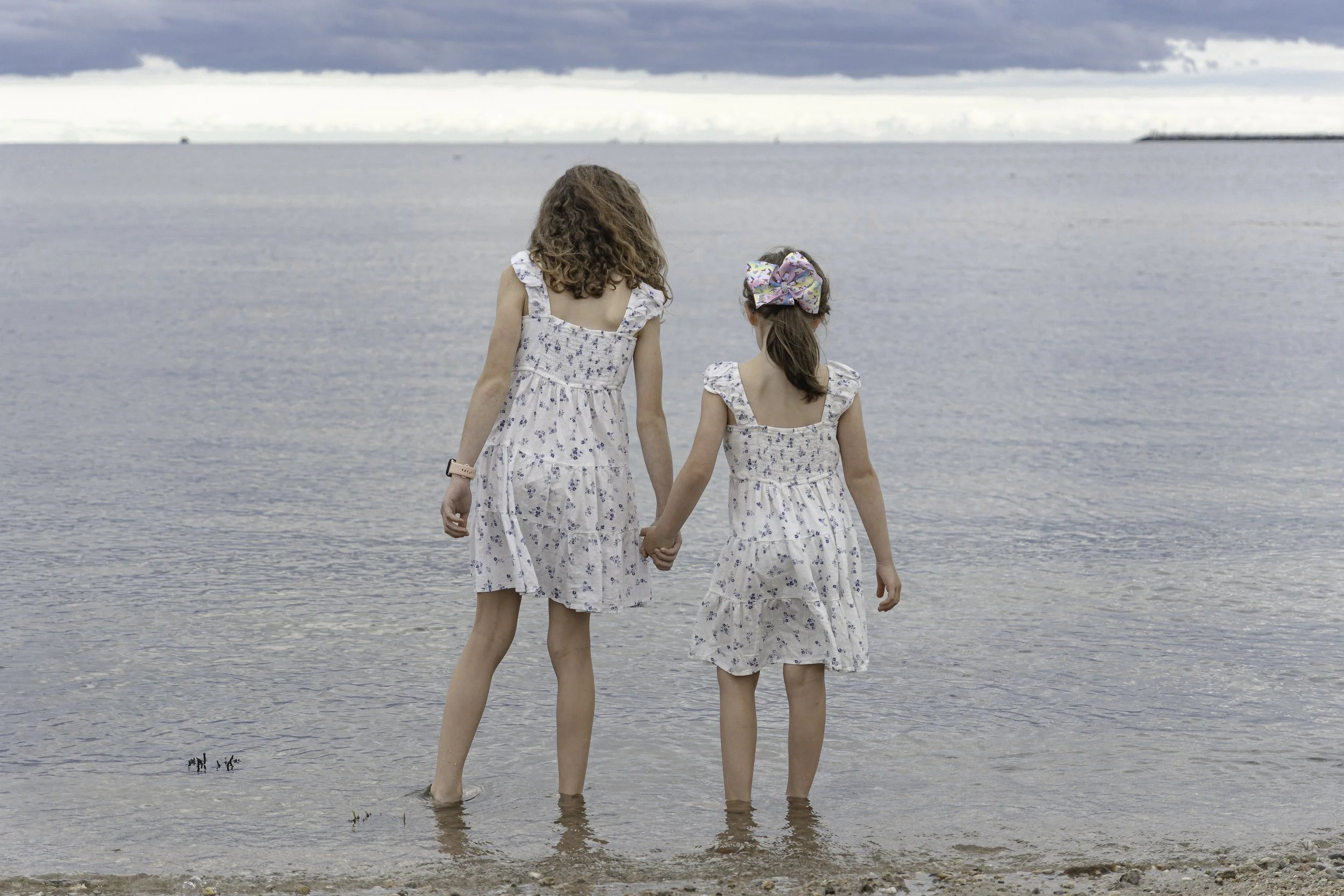 Sisters walking hand in hand along the shoreline during a relaxed family photo session in Massachusetts.