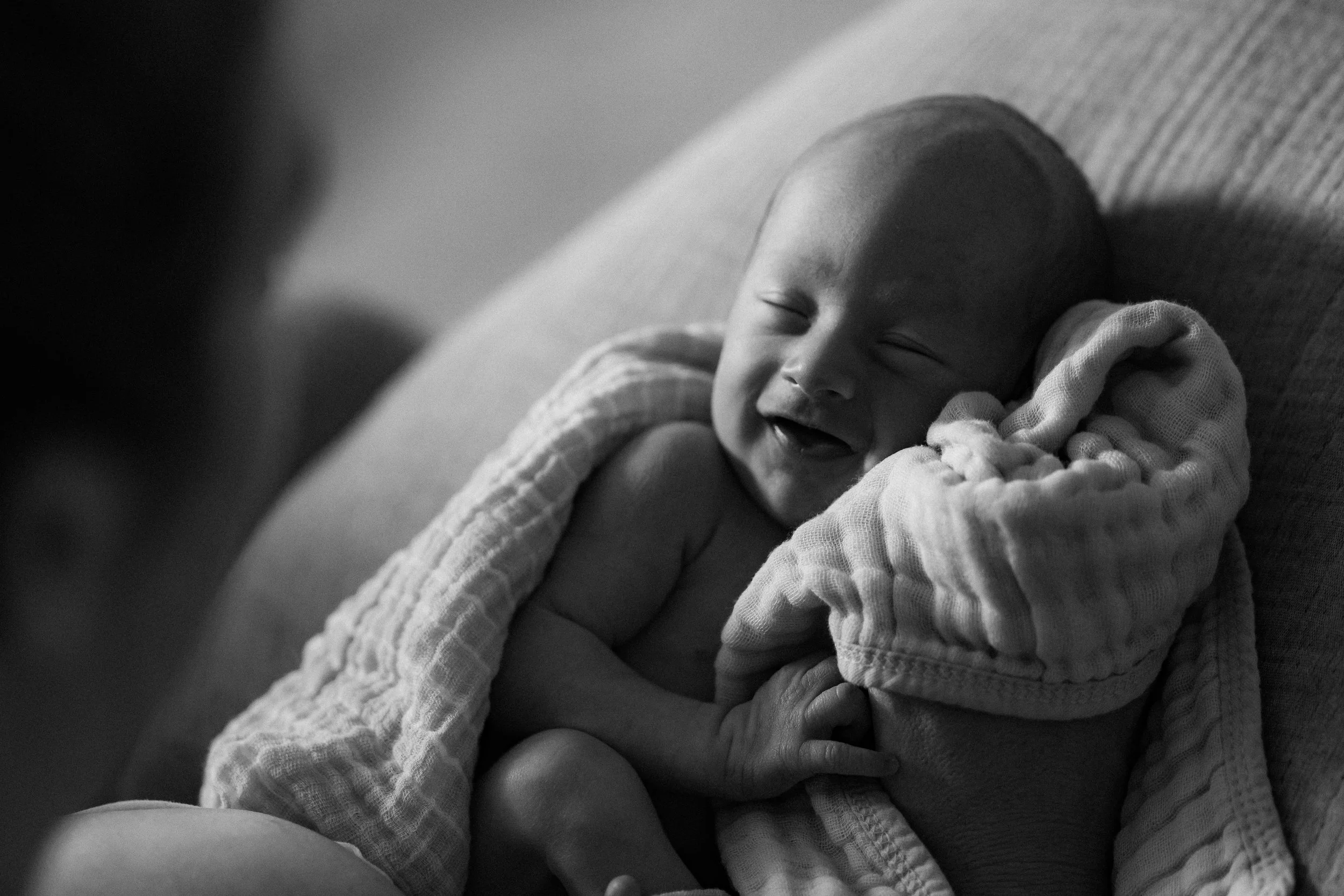 Intimate black and white image of a newborn smiling while cradled during a lifestyle photography session in Central Massachusetts.