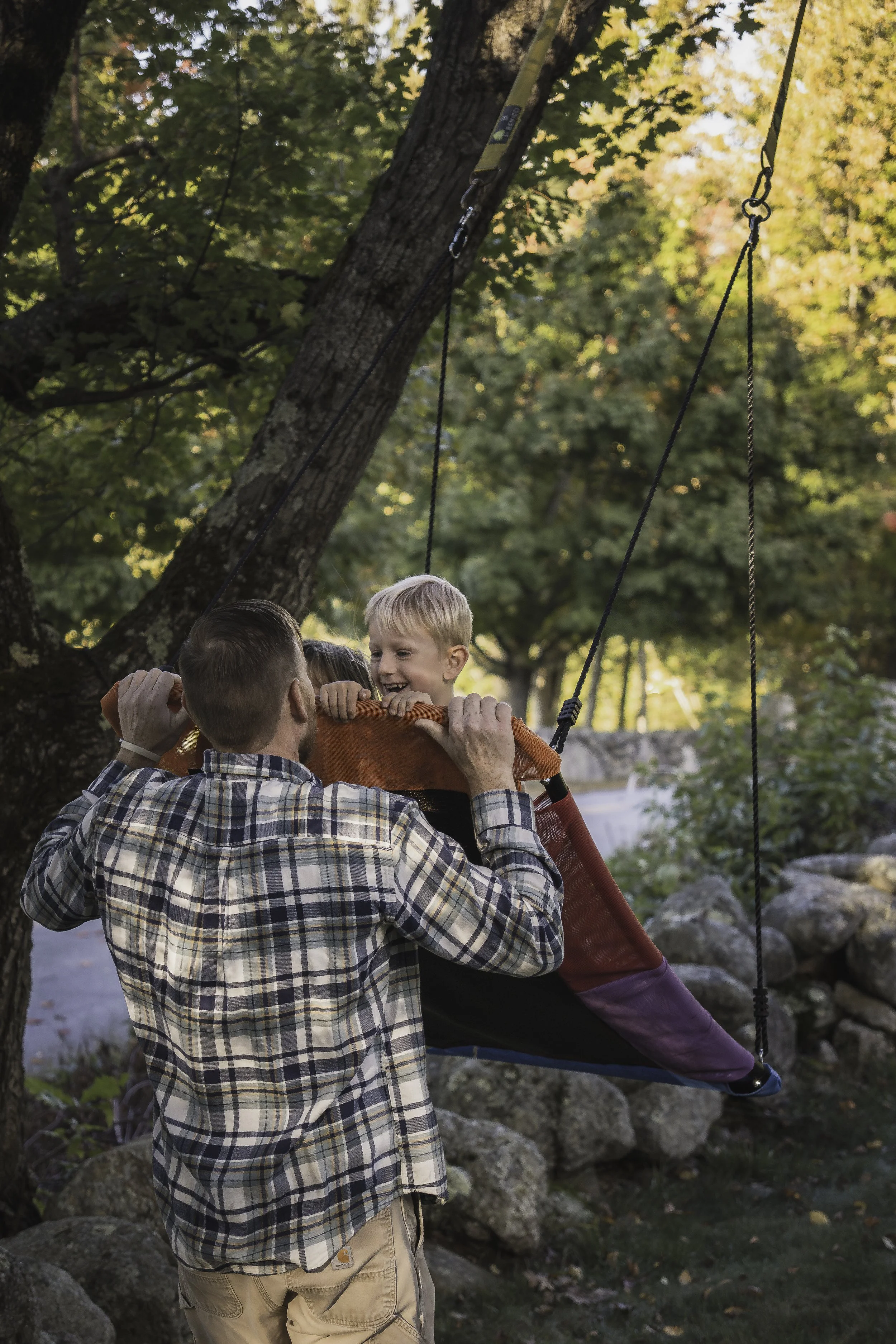 Father pushing son on a wooden swing surrounded by fall foliage during family photography session near Leominster