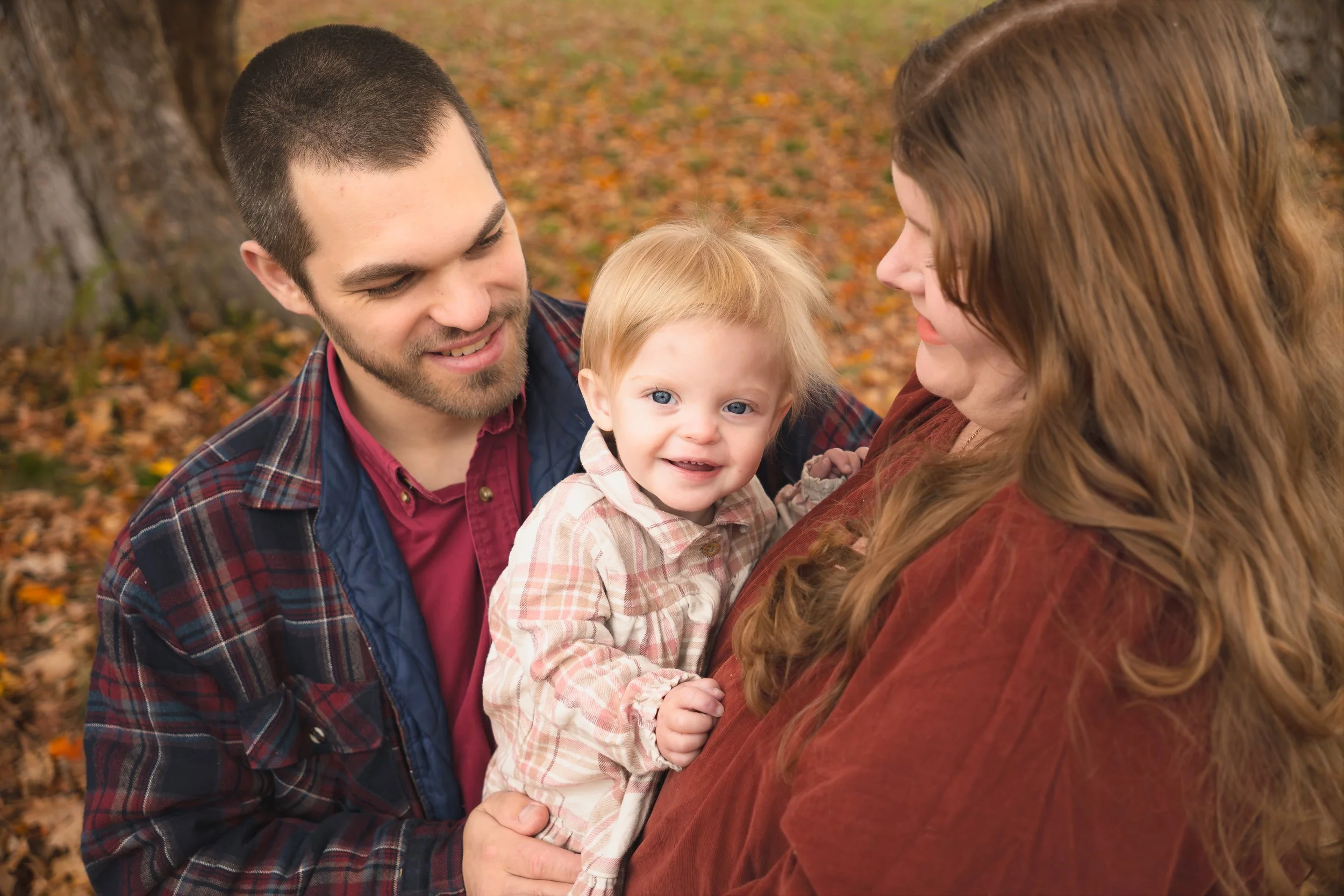Parents smiling and holding baby during cozy fall family portrait session near Concord Massachusetts. 