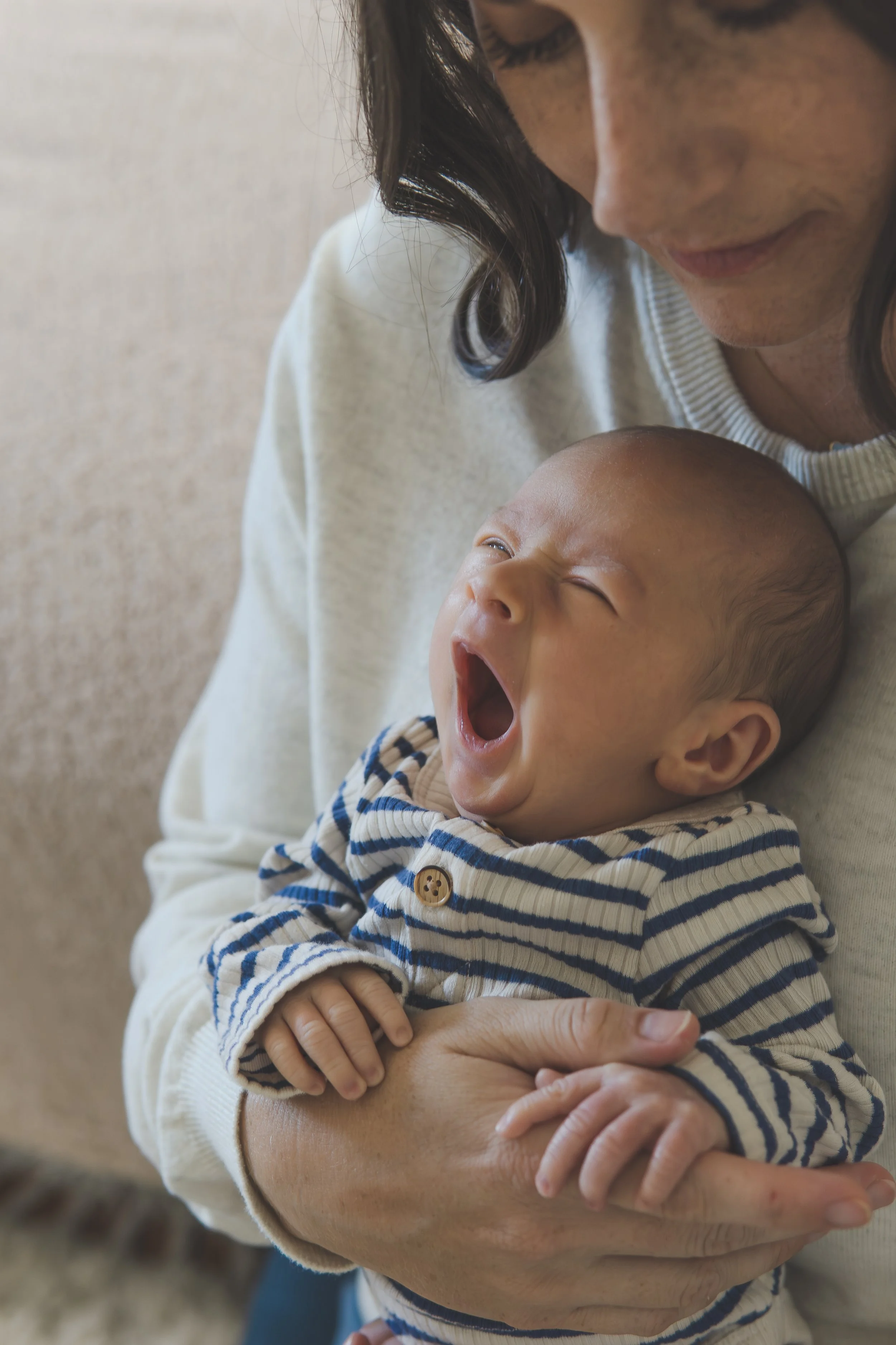 During a lifestyle family newborn photo session in Newburyport  a young mother holds her yawning baby.
