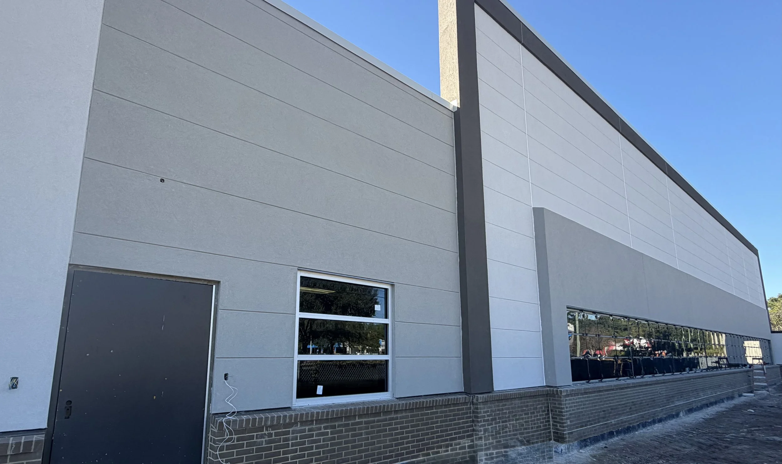 Modern commercial building with large windows and a brick base, under a clear blue sky.