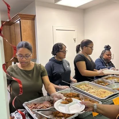 Four women serving food at a buffet table indoors.