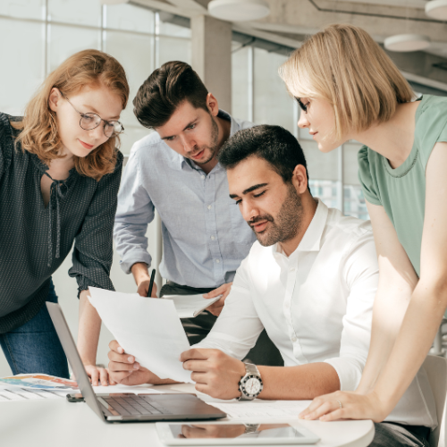 Four professionals gathered around a laptop, discussing documents in a modern office.