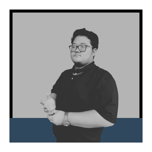 A young man wearing glasses and a dark polo shirt, standing with his arms crossed against a plain background.