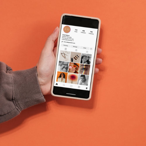Person holding smartphone displaying an Instagram profile against an orange background.