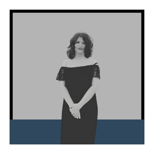 A woman with shoulder-length curly hair wearing an off-the-shoulder black dress standing against a plain background.