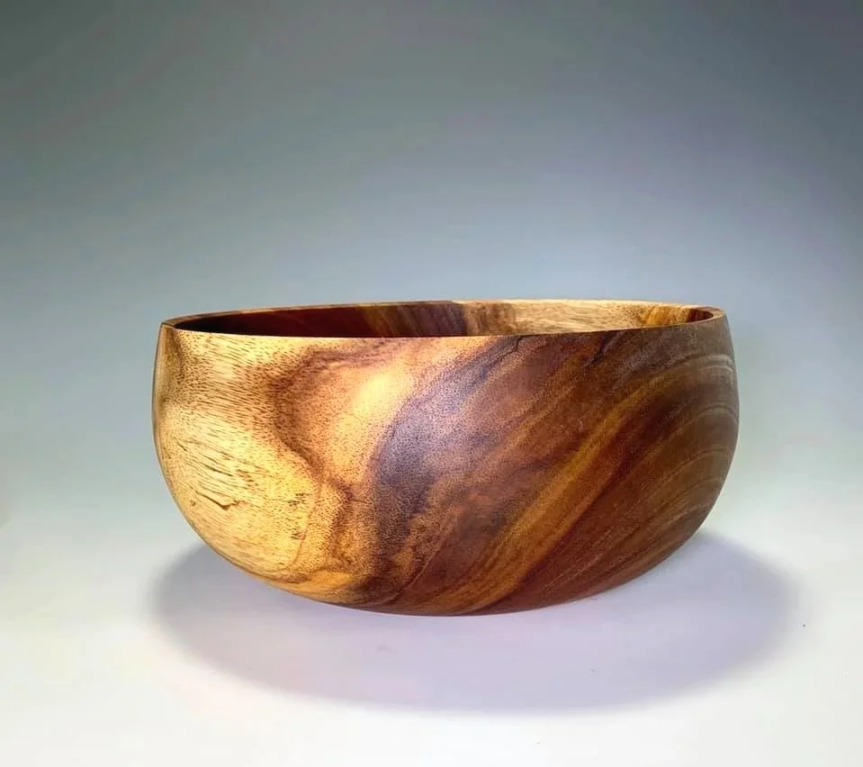 A Hawaiian native Milo wood bowl with natural grain patterns, resting on a white surface against a gradient background.