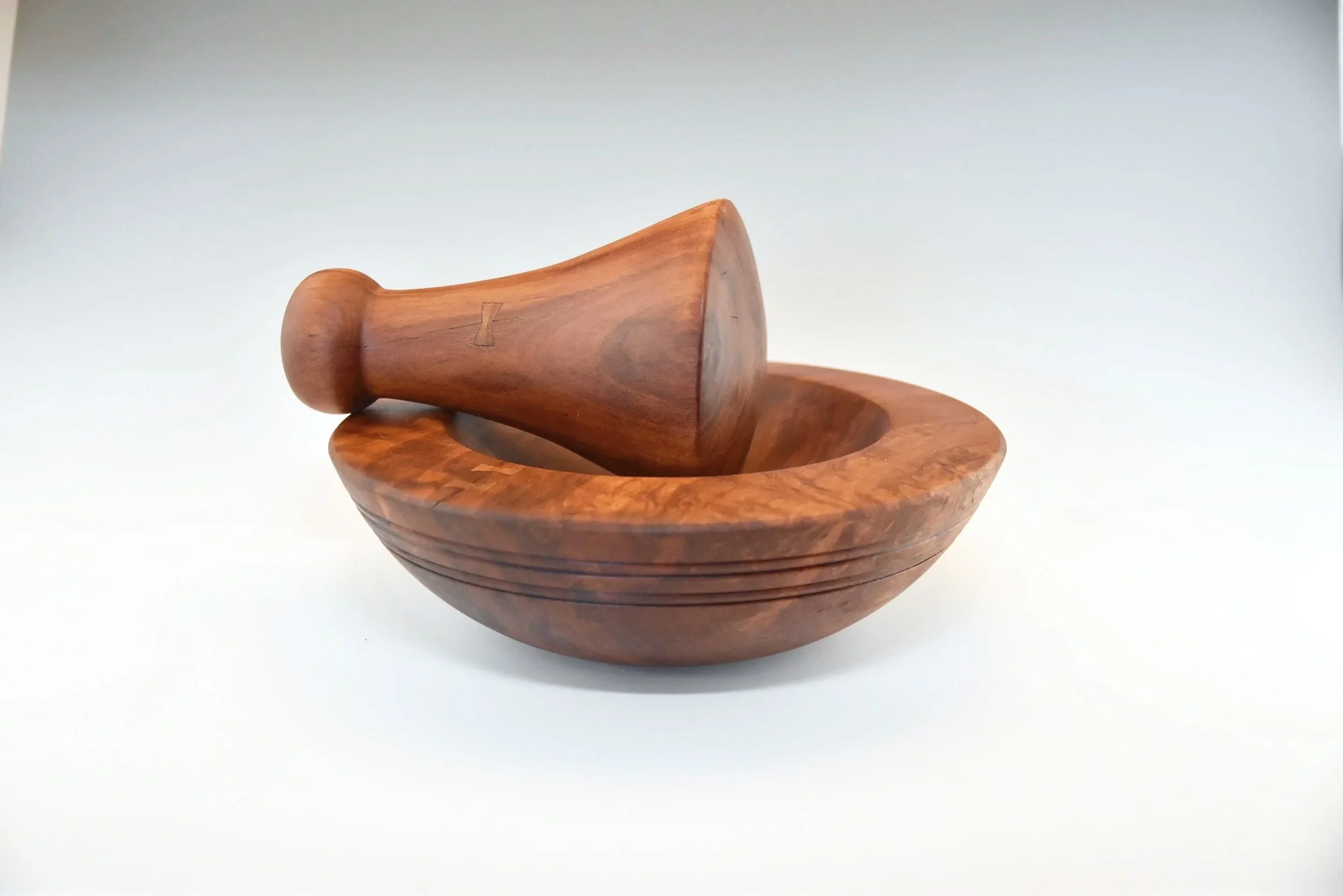 A wooden Hawaiian mortar and pestle set, with the pestle resting inside the mortar on a white background.