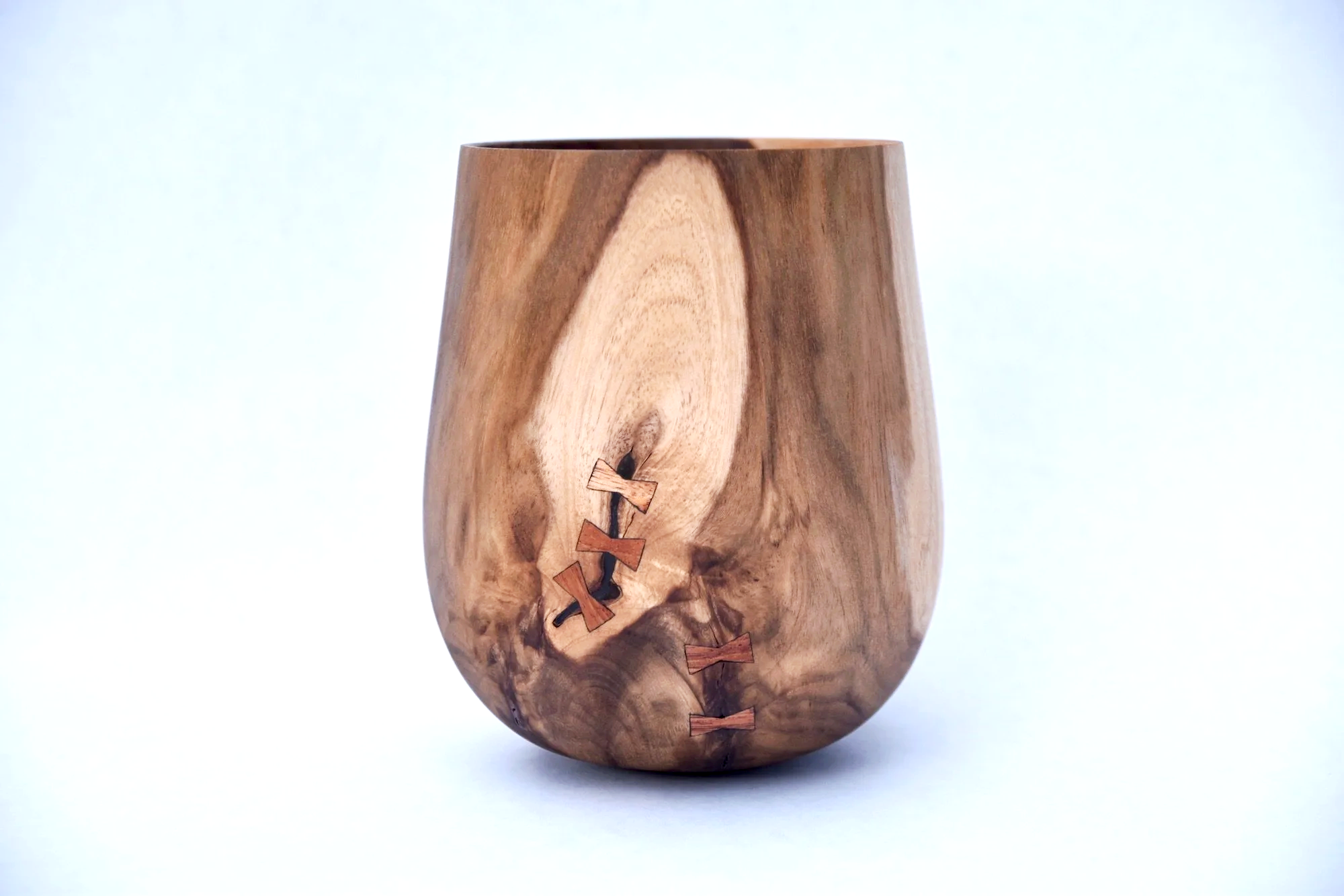 A wooden vase with a natural wood grain pattern and small bowtie-shaped inlays along a dark line.