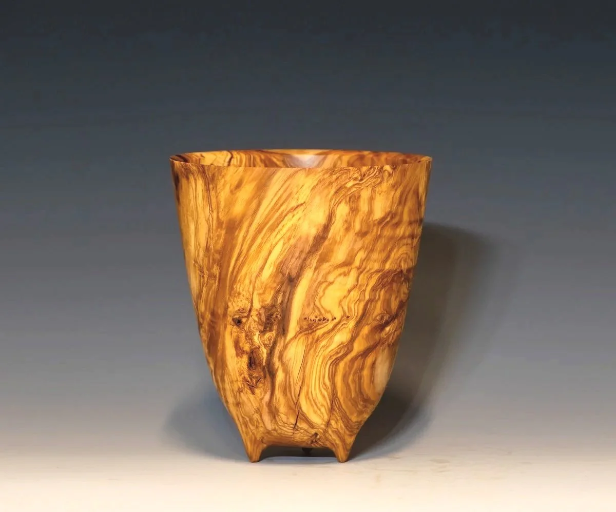 A wooden vessel with a marbled pattern in amber and brown tones, standing on a flat surface against a neutral background.