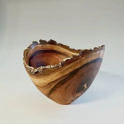 A wooden bowl with a natural, uneven edge and wood grain patterns, placed against a plain background.