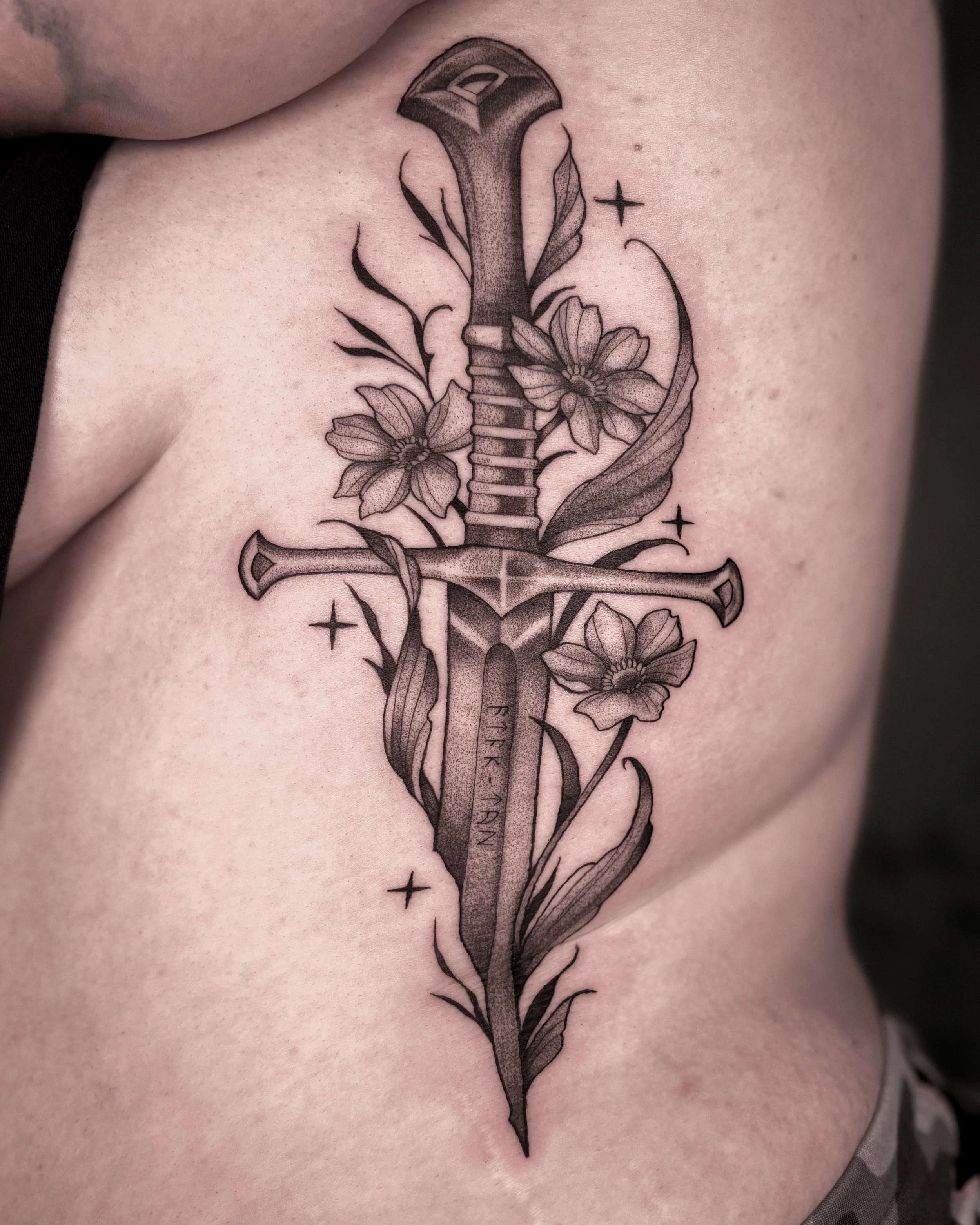 Tattoo of a sword with flowers and stars on skin.