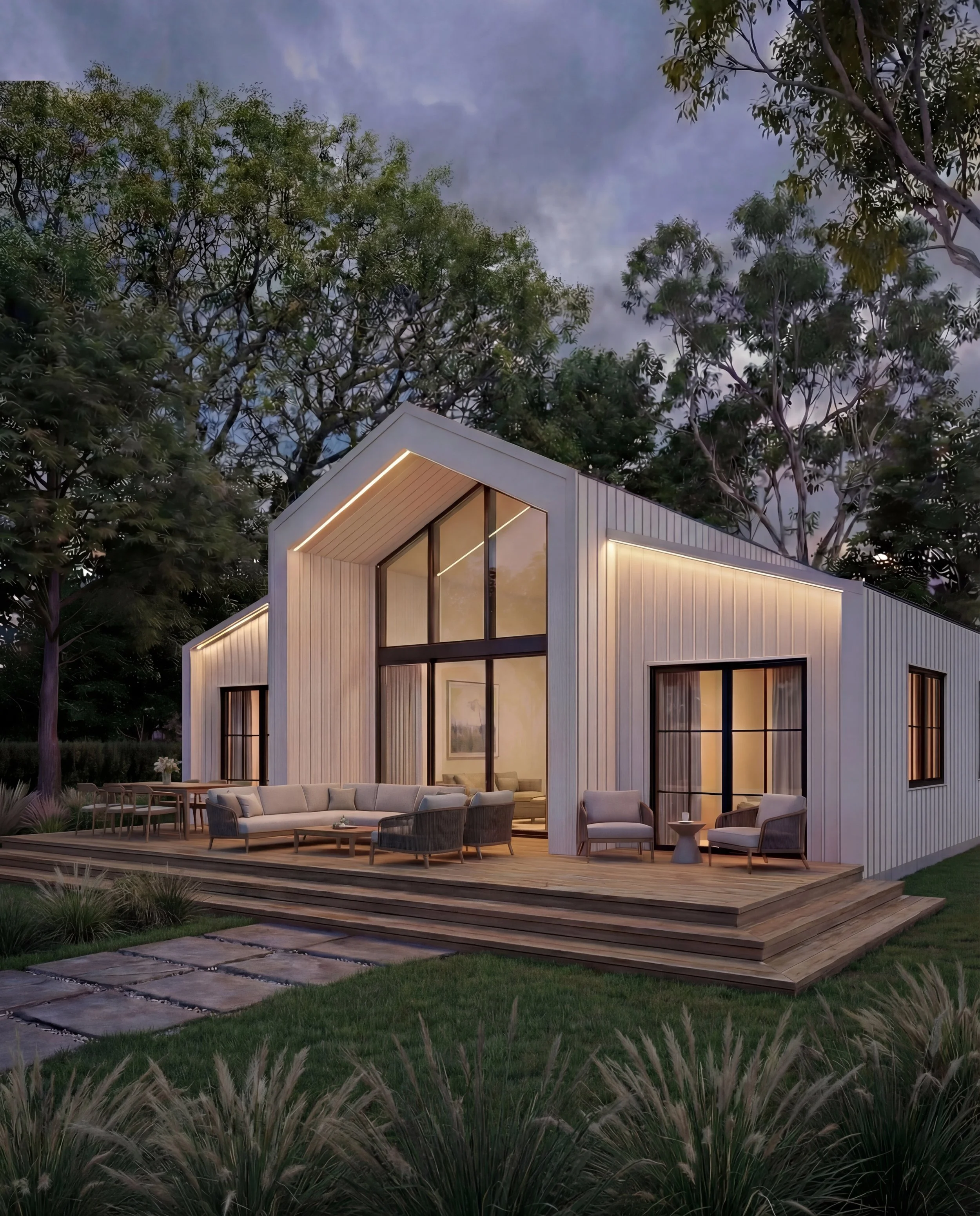 Modern house with large windows and a wooden deck, outdoor seating area, surrounded by trees during dusk.