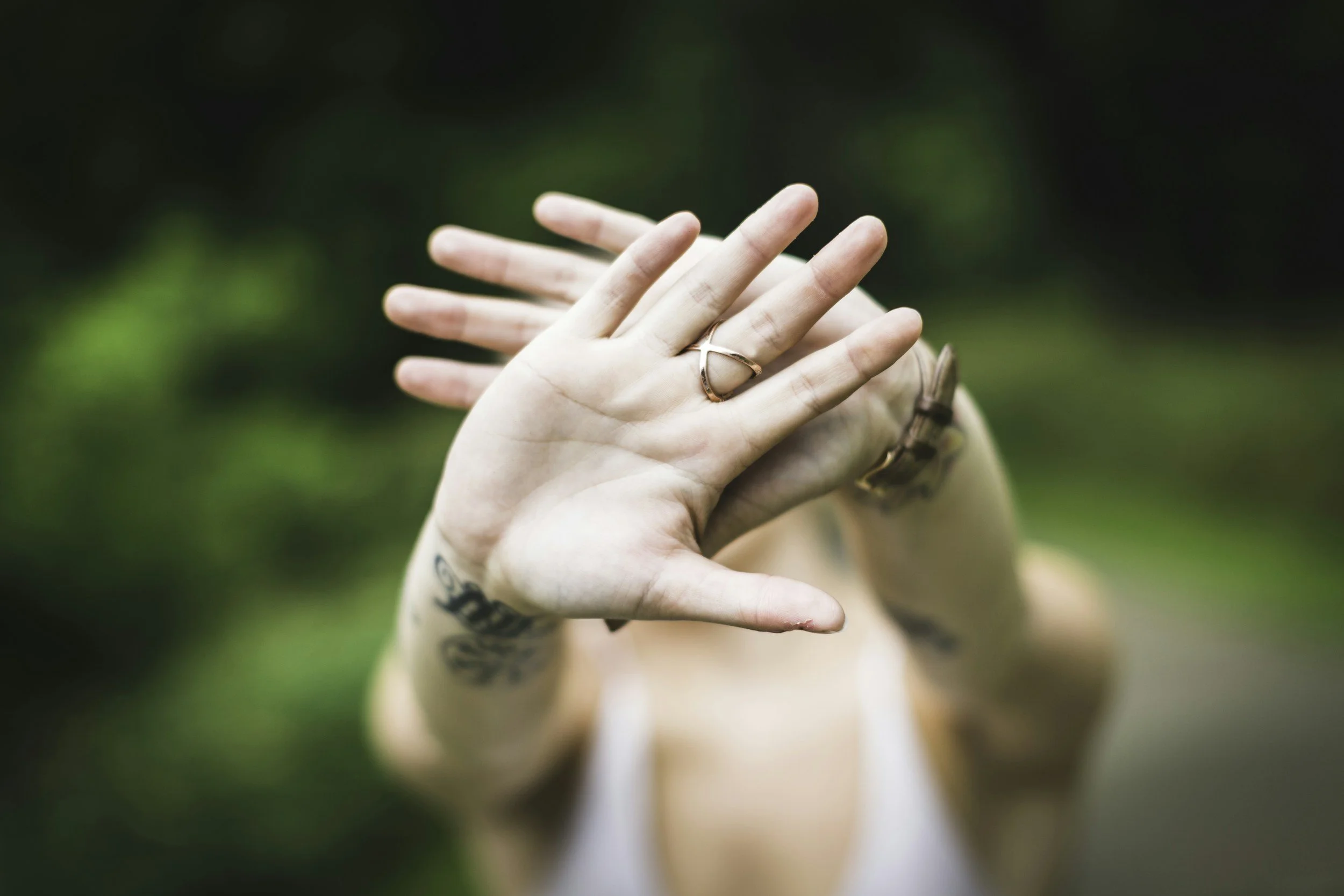 Selective focus photo of a person's hand with a ring, hiding their face.