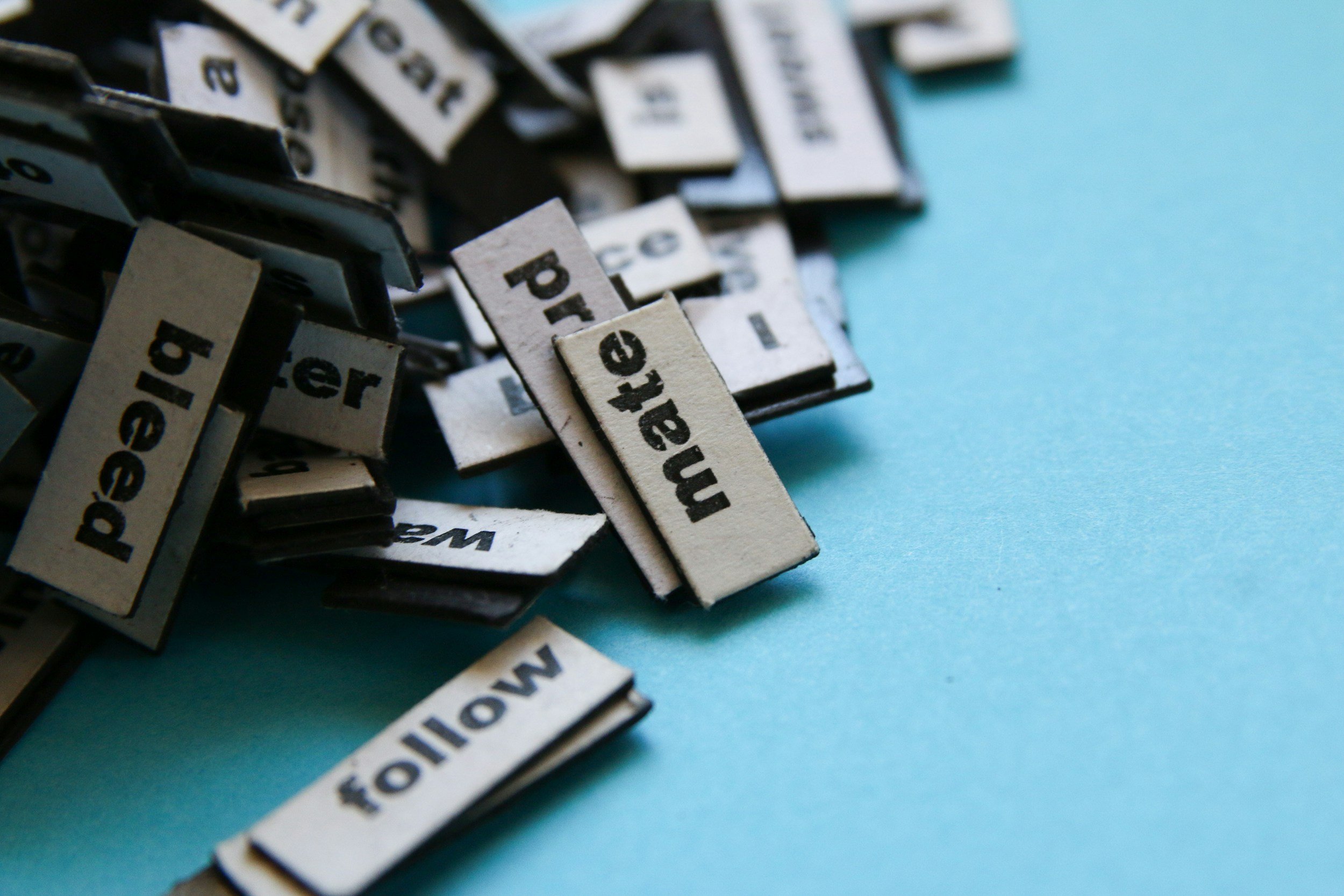 A pile of typed word magnets jumbled together on top of a blue surface.