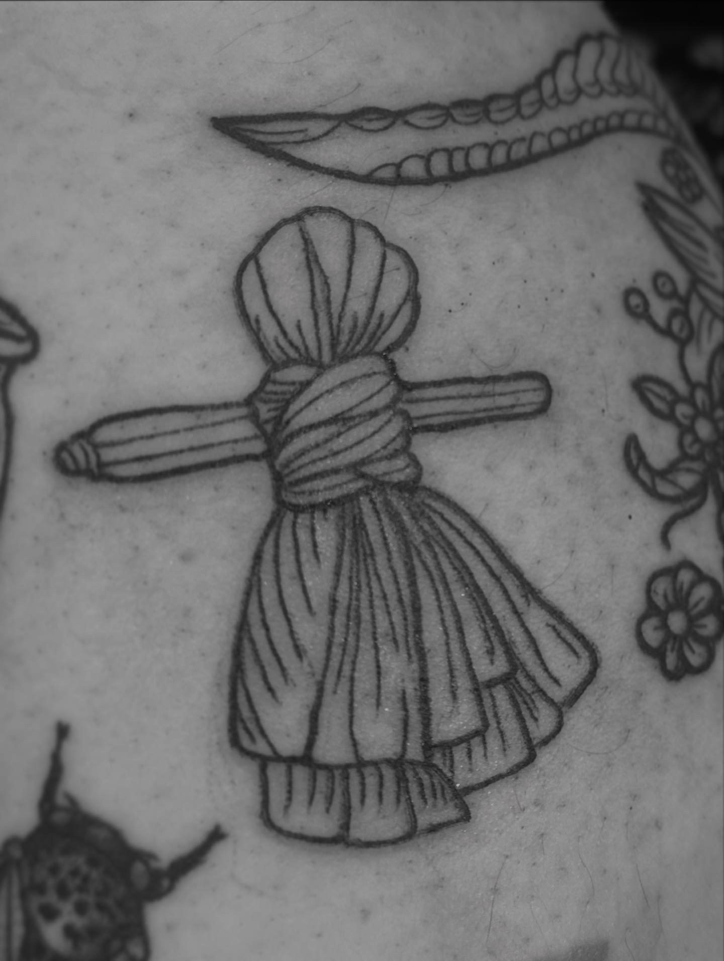 Black ink tattoo of a corn dolly.