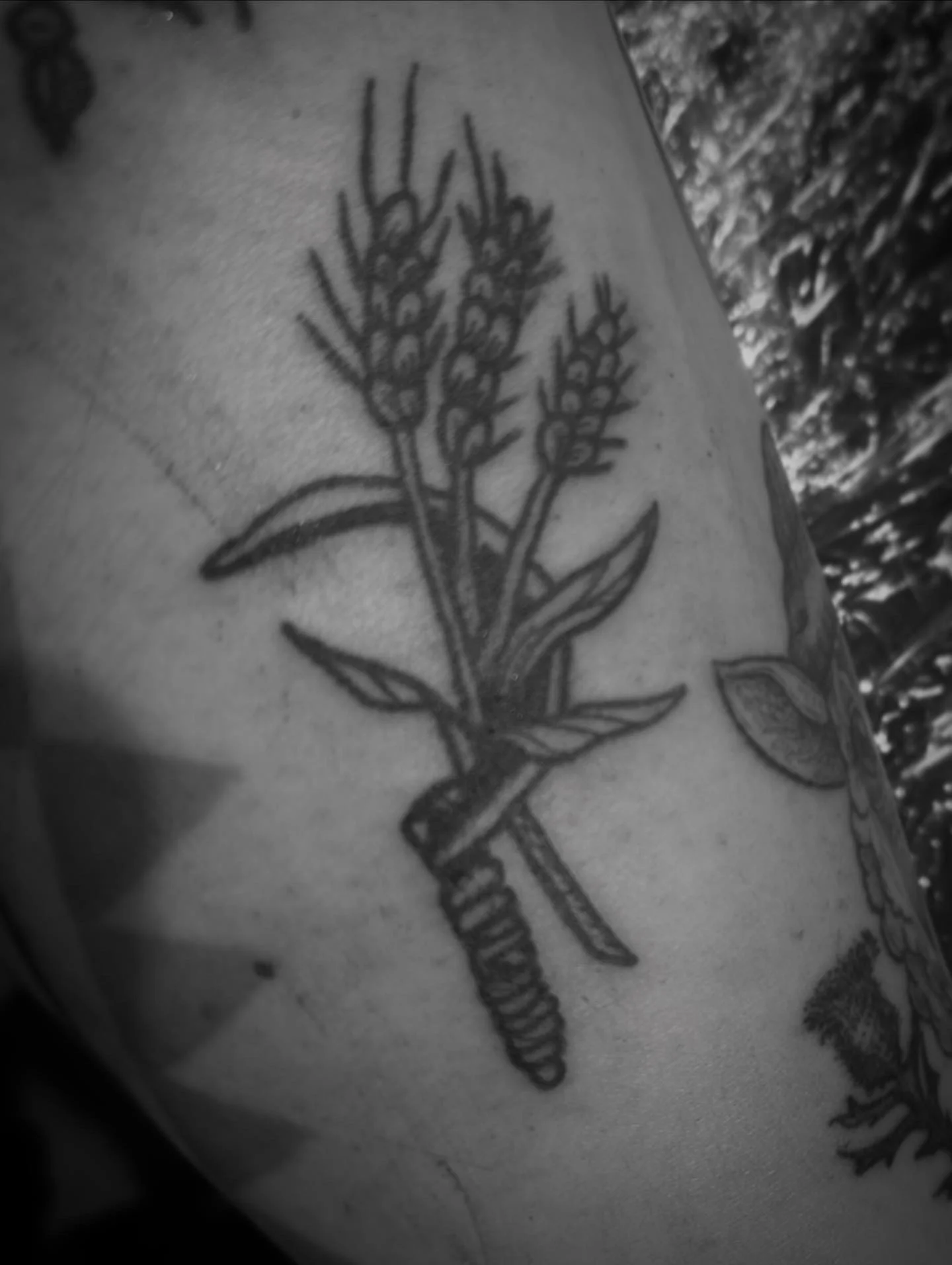 Black ink tattoo of a scythe and wheat.