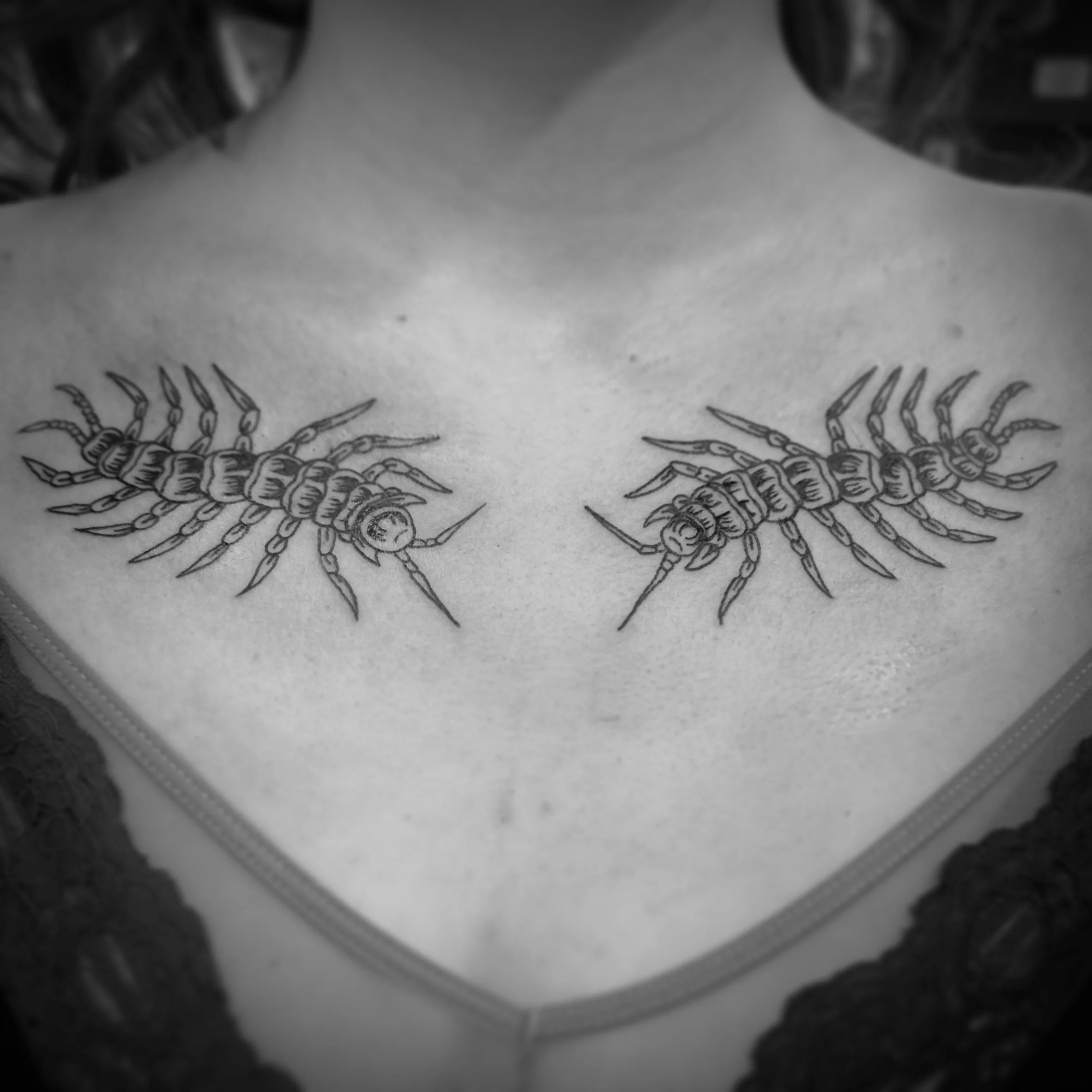Black ink tattoo of collarbone centipedes.