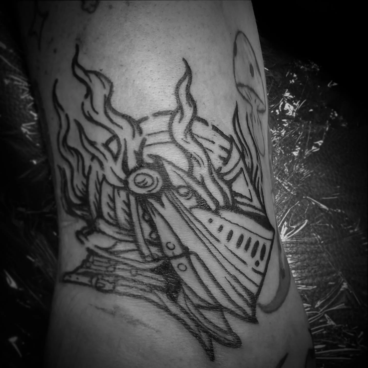 Black ink tattoo of a flaming knight helm.