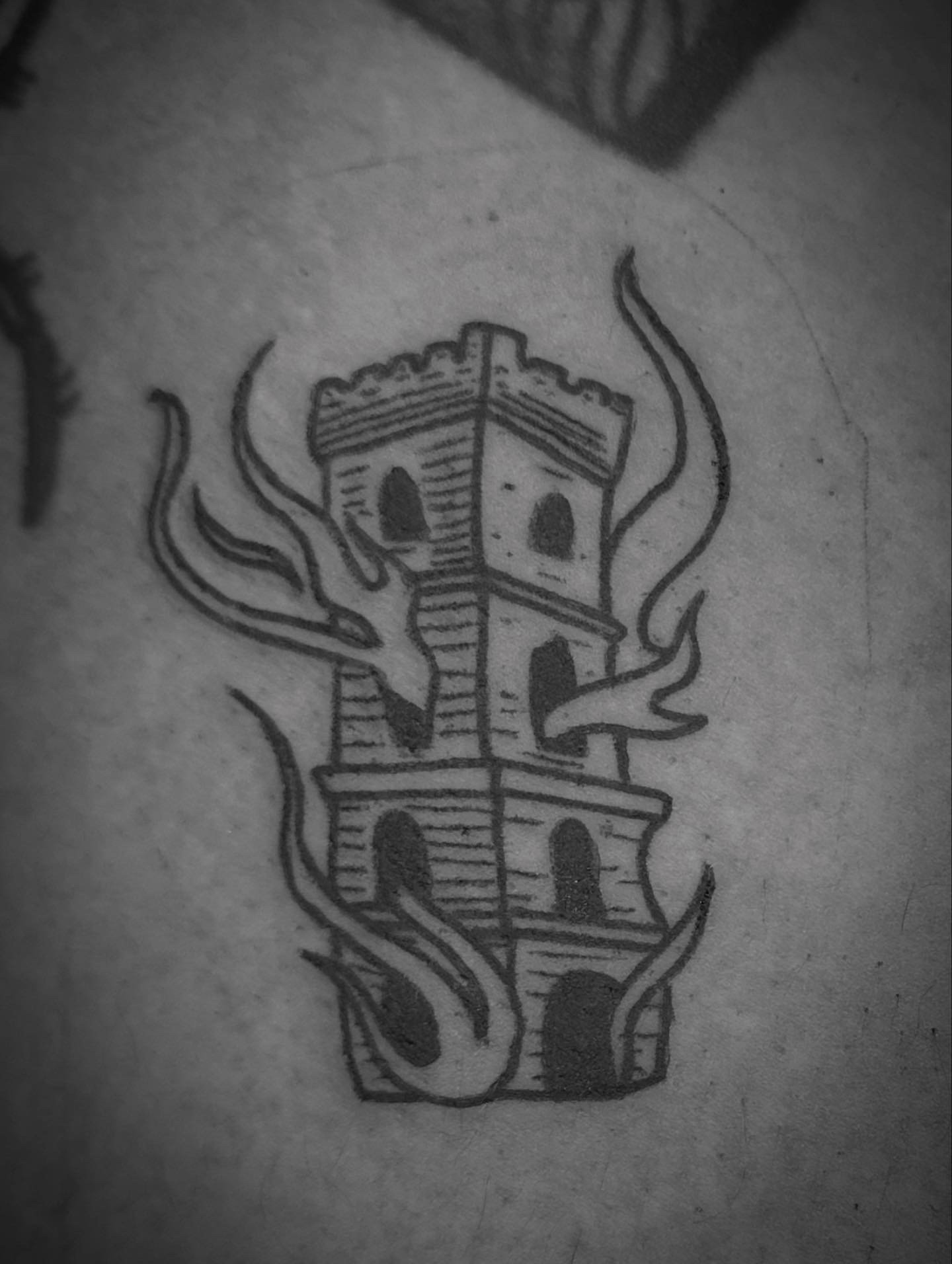Black ink tattoo featuring a burning castle tower.