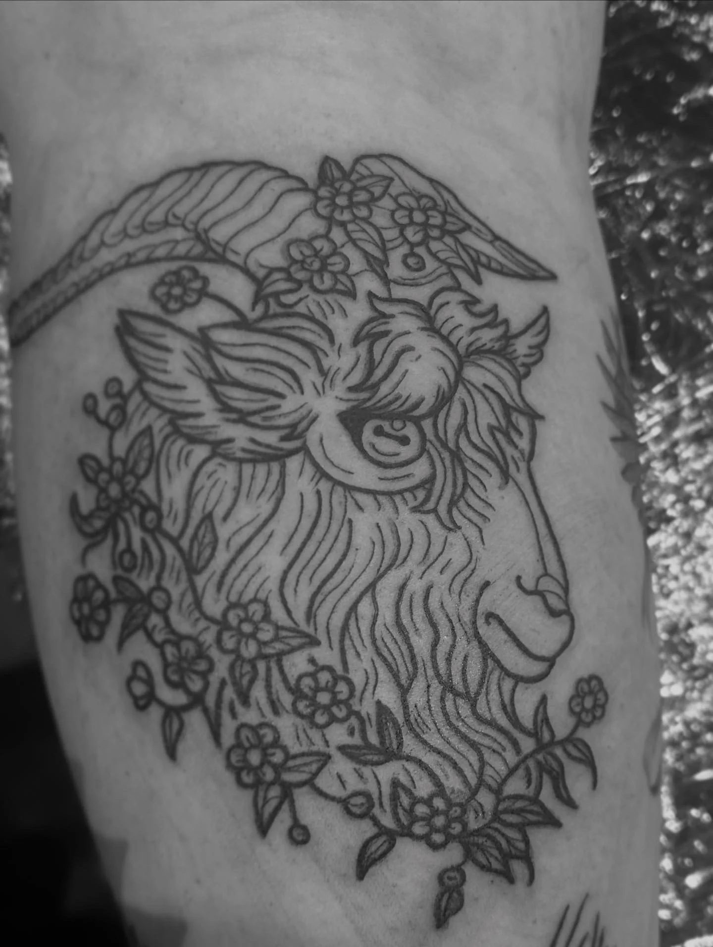Black ink tattoo of a goat with a flower crown.